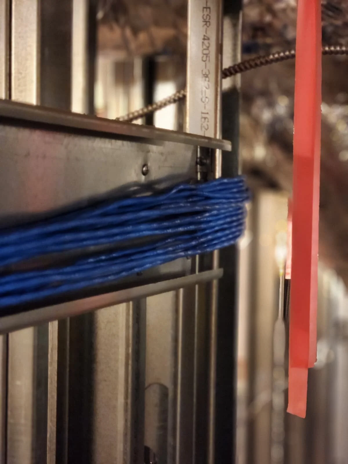 Close-up view of a mechanical structure with metal rods, wires, and a pink paper tab on the right side.