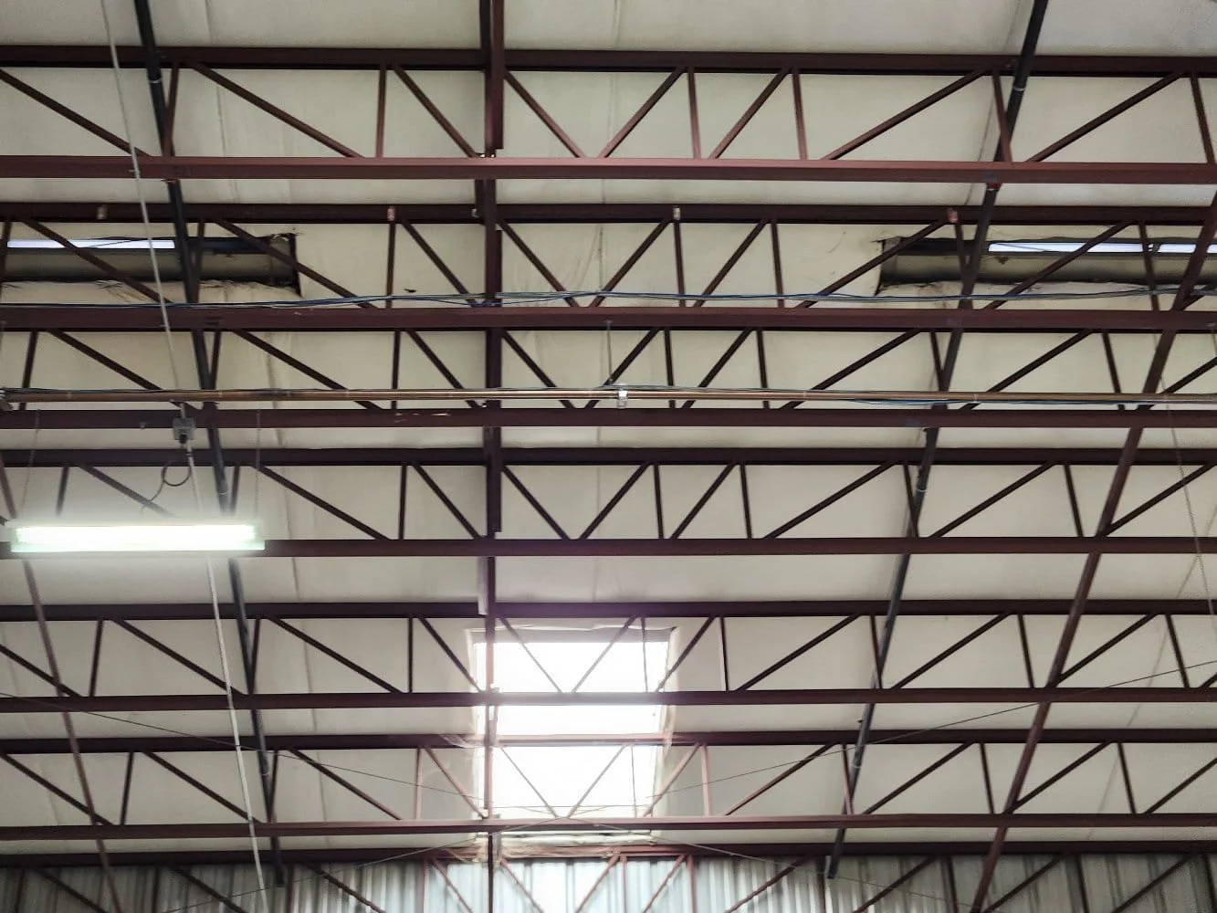 Ceiling of a warehouse with metal truss framework, skylight, and fluorescent lighting