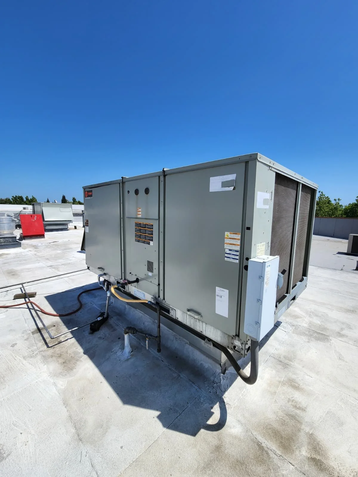HVAC rooftop unit on a flat rooftop under a clear blue sky.