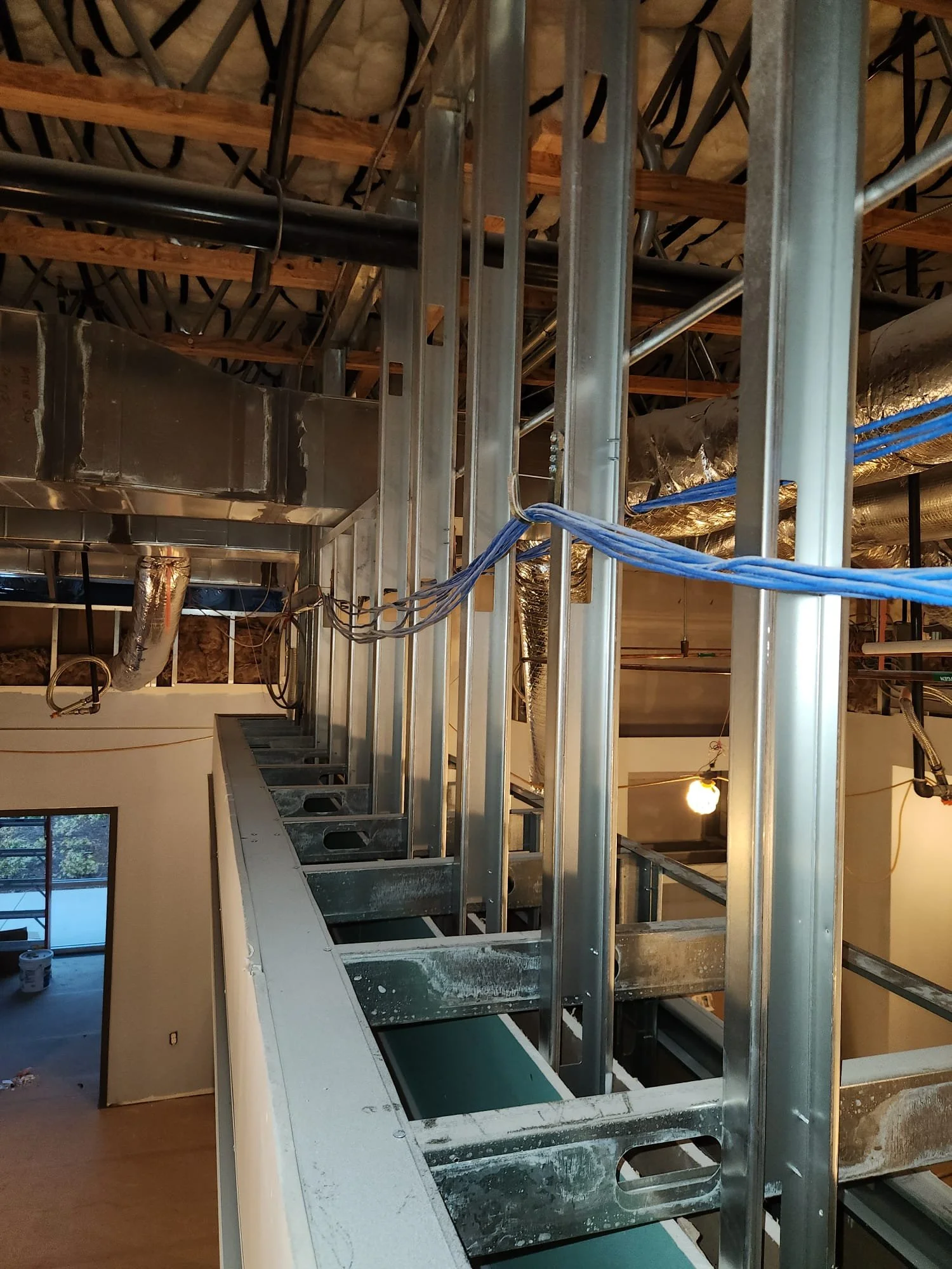 Interior view of a building under construction with exposed metal framing, electrical wiring, and ductwork.