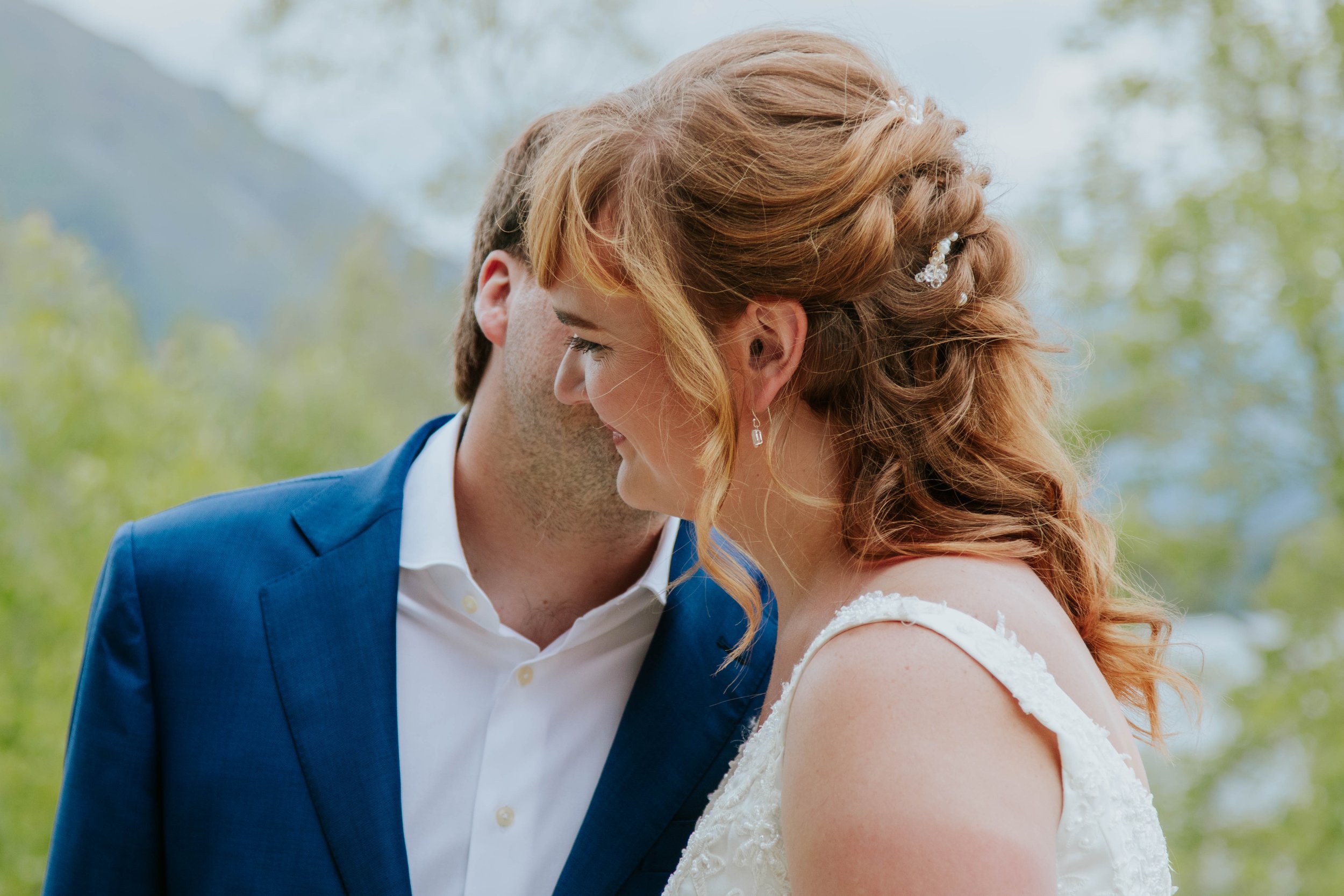 Bride and groom close together outdoors, leaning their foreheads on each other smiling.