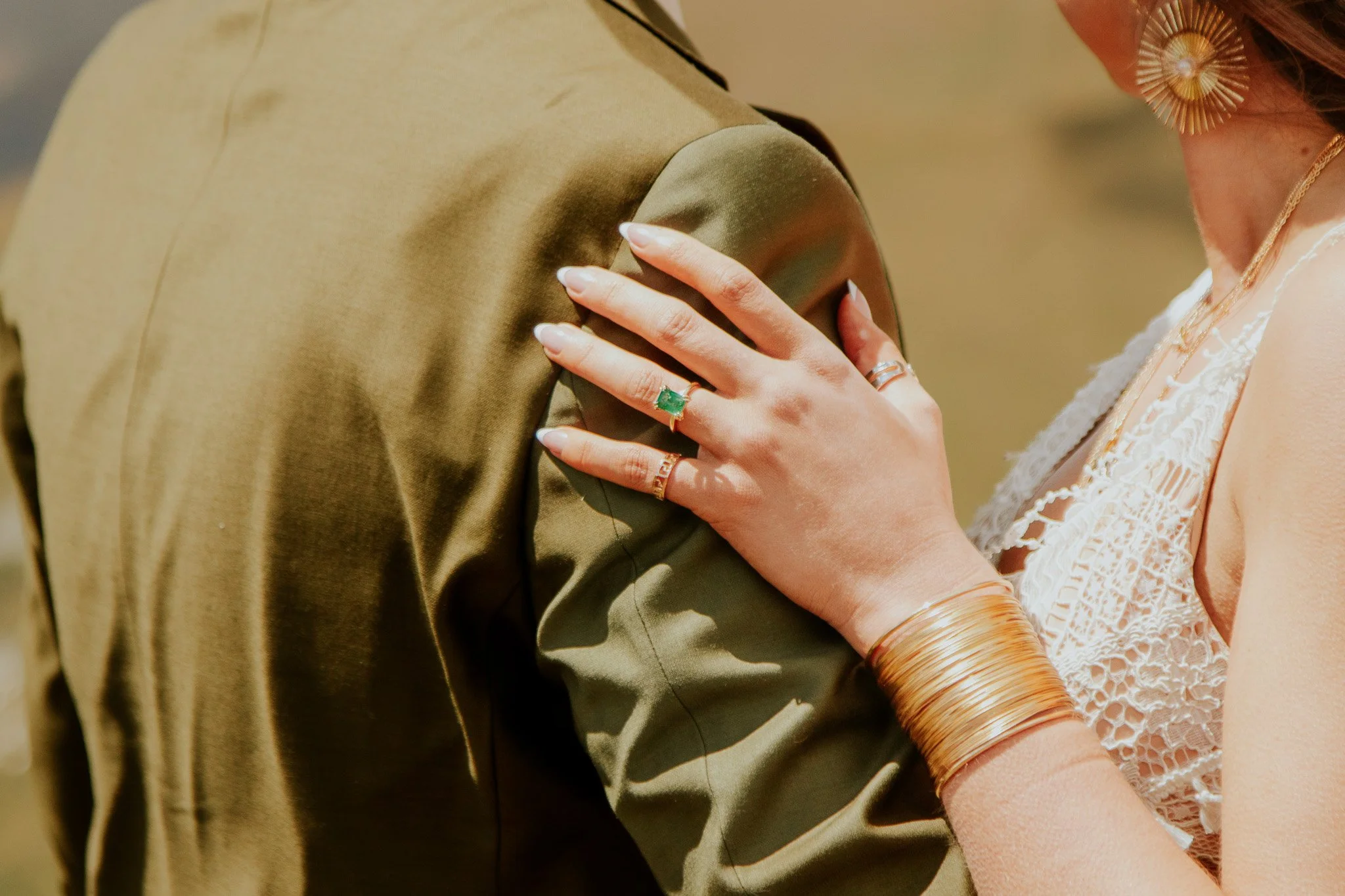 A woman wearing a lace dress with gold jewelry, touching a man in a green jacket.