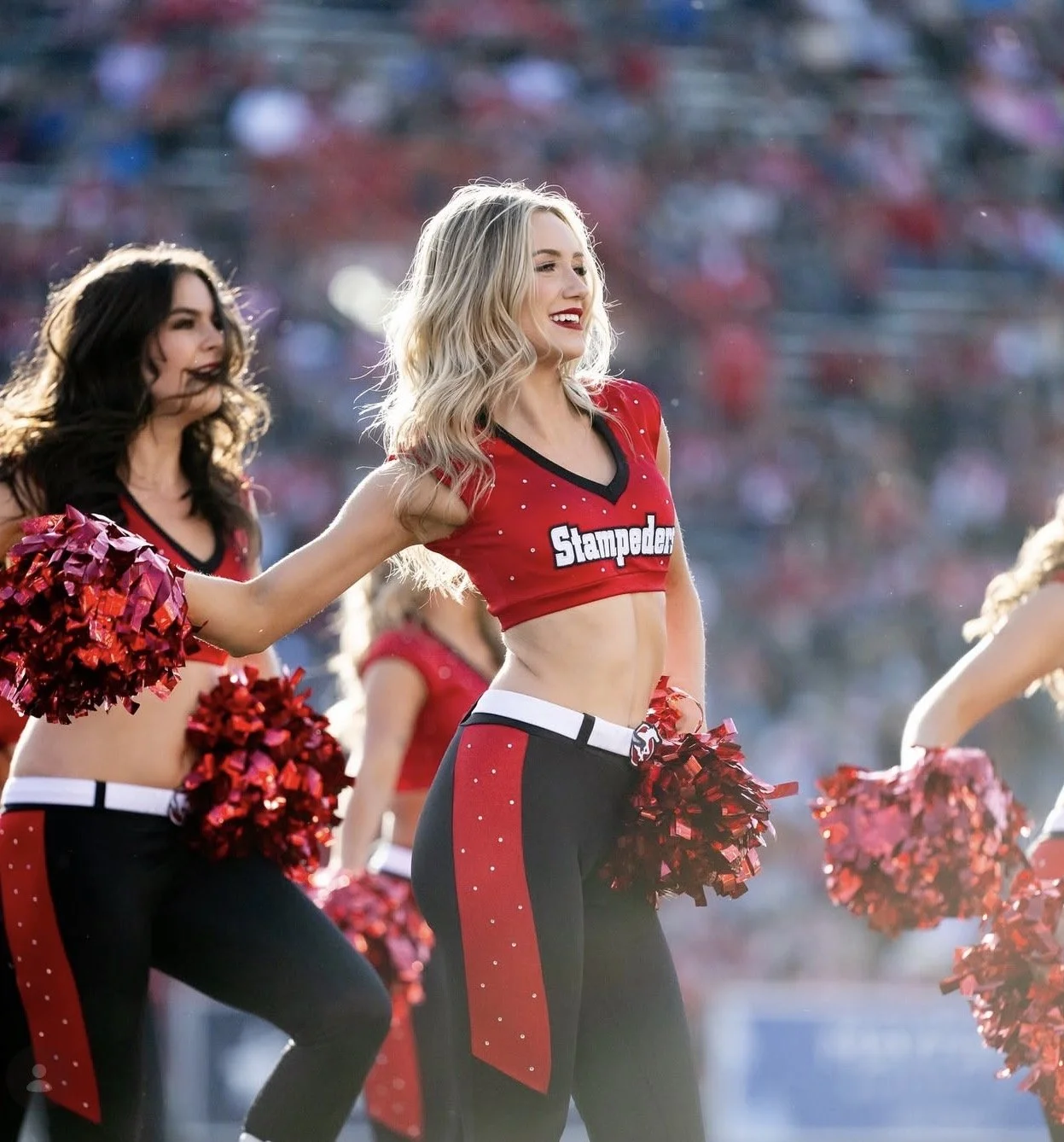 Cheerleaders performing during a football game, wearing red and black uniforms with pom-poms.