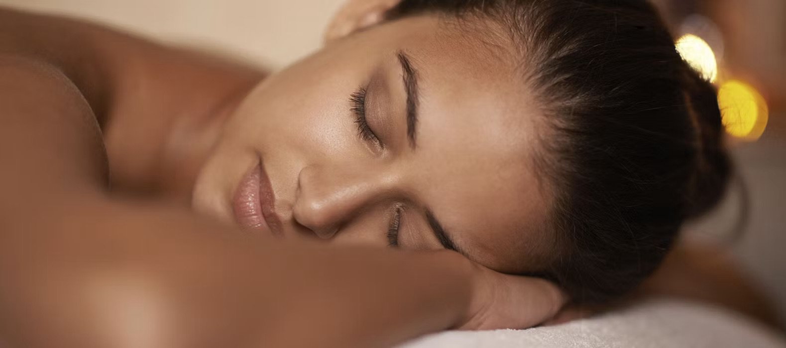 A woman with closed eyes lying on her side with her head resting on her arm, appearing relaxed.
