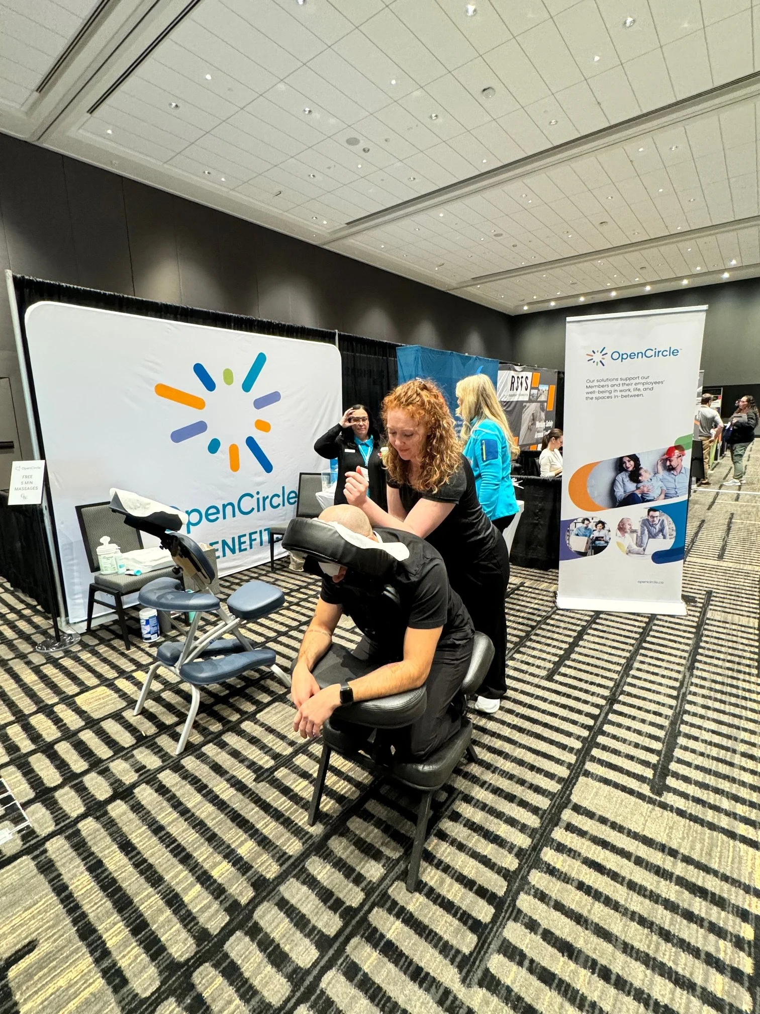 A person receives a massage at a booth with OpenCircle branding during a conference.