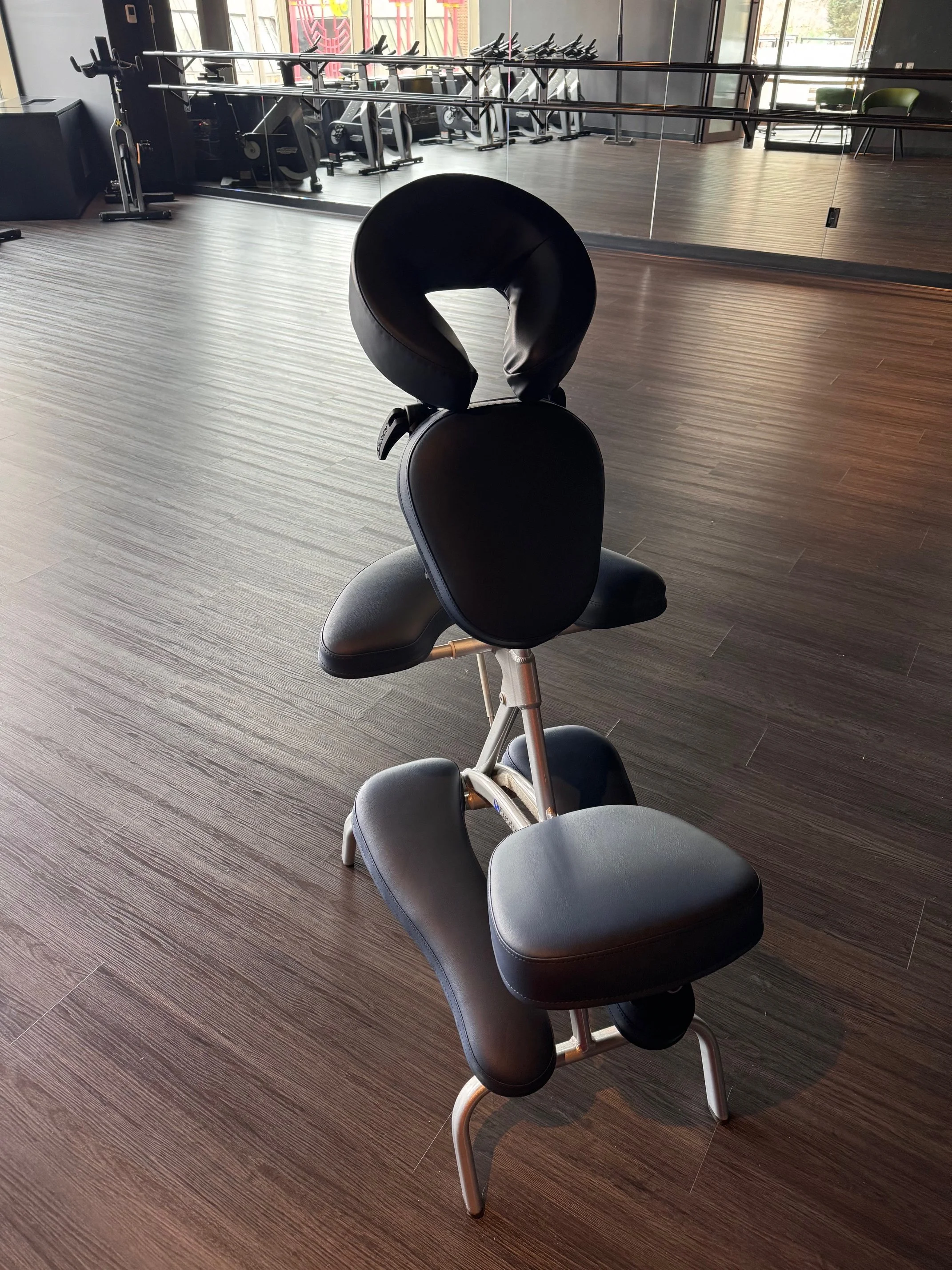 A specialized ergonomic chair with head and waist supports in a gym or fitness studio with mirrors and exercise equipment in the background.