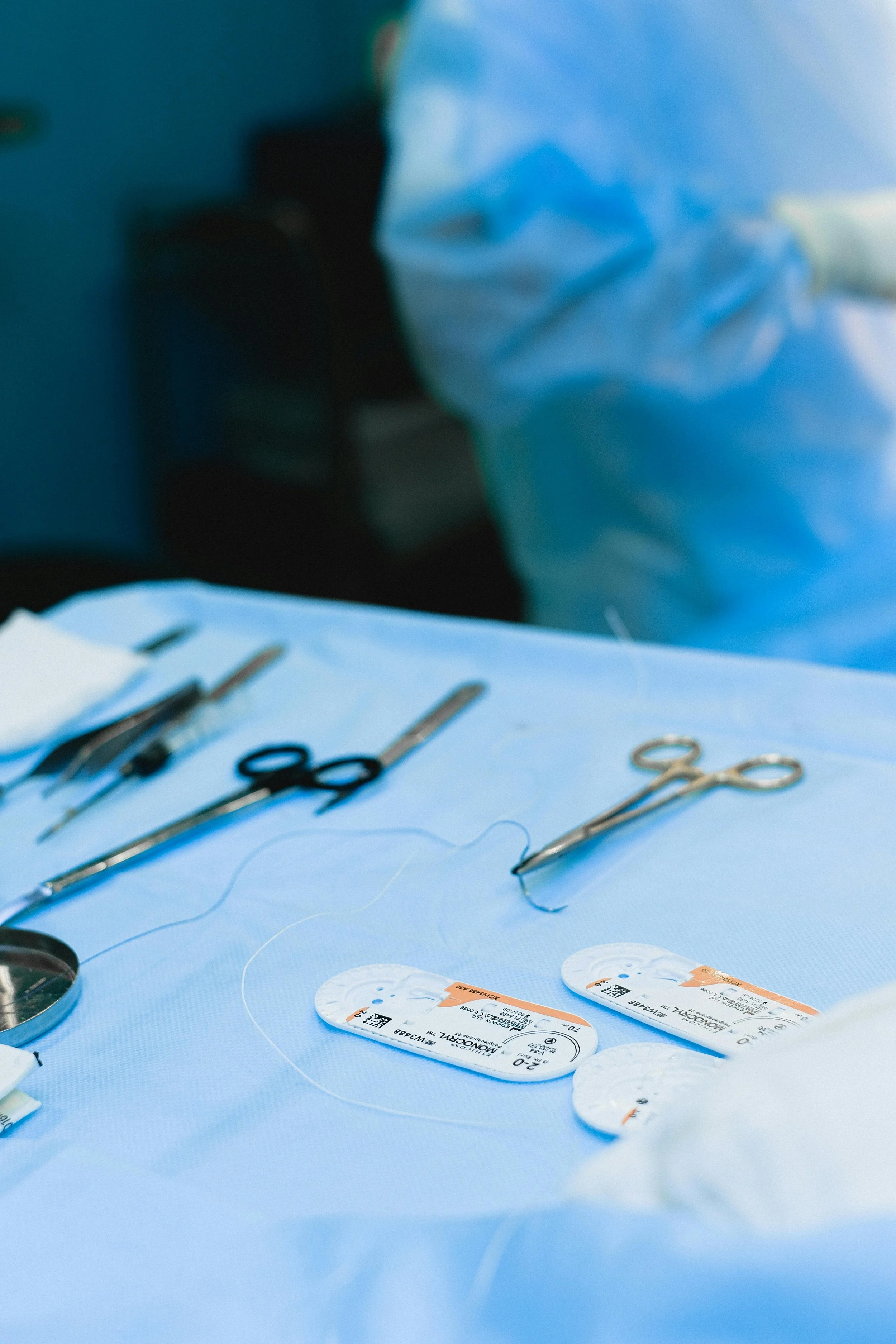Medical surgical tools on a blue sterile drape, including pacemaker devices and scissors, in a surgical setting.