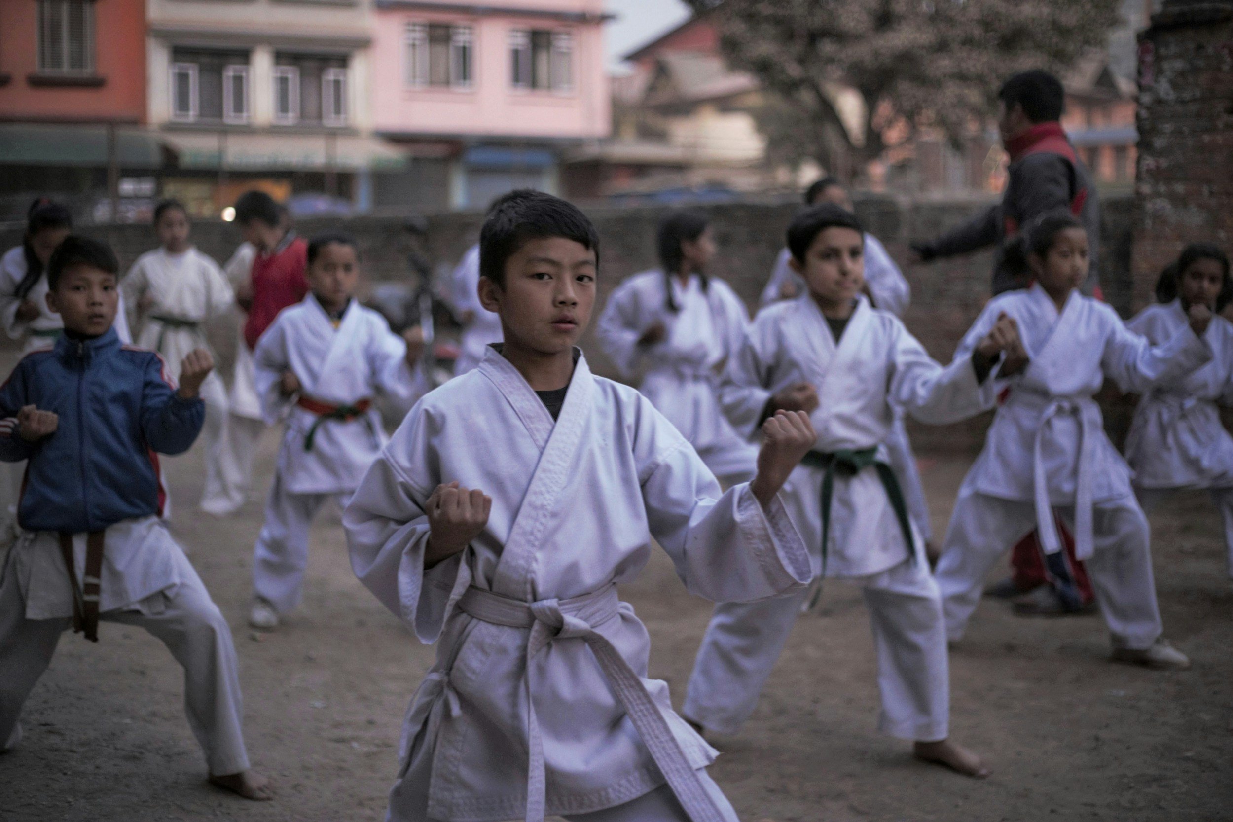 Children practicing martial arts outdoors, dressed in traditional karate uniforms with belts, in a group training session.