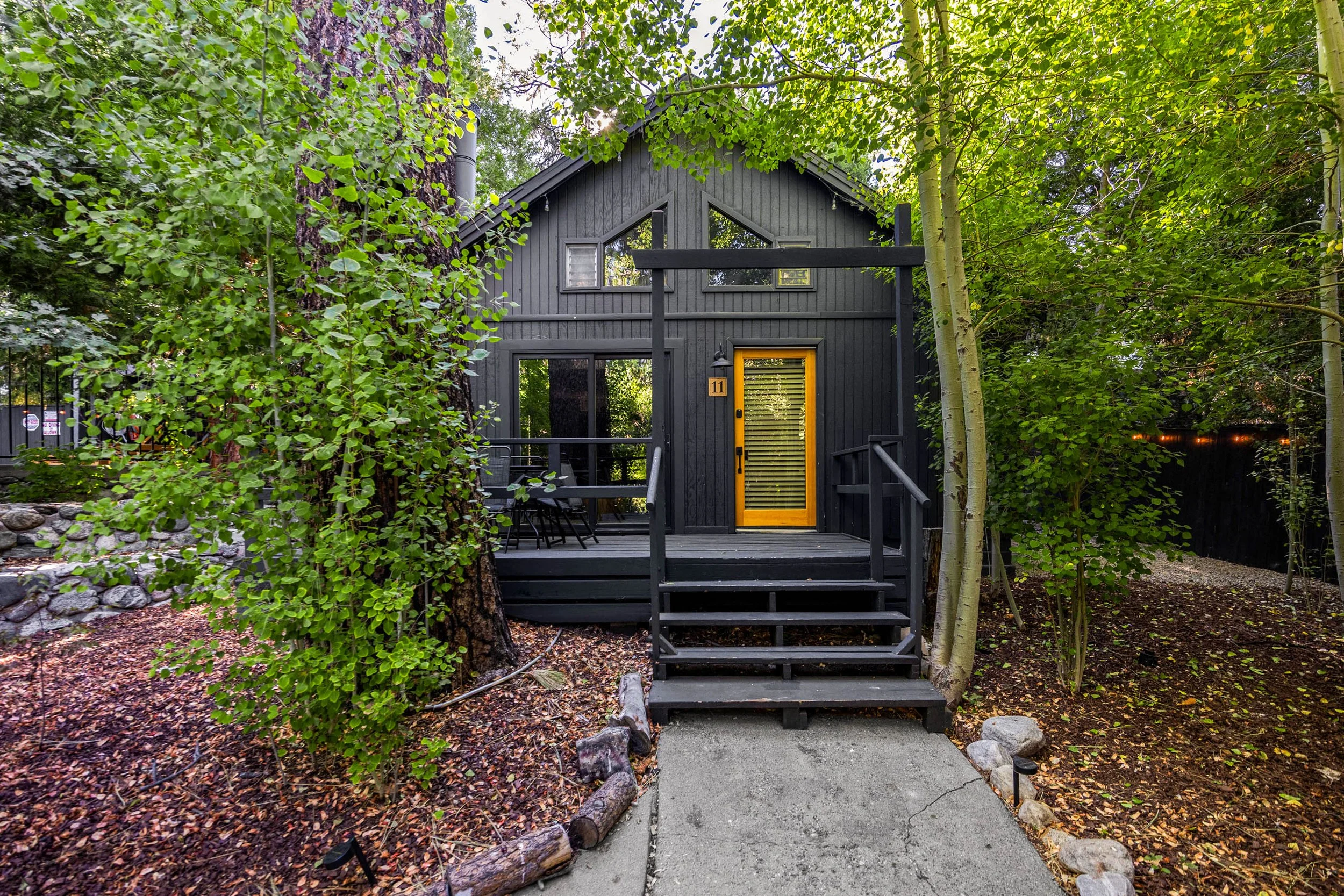 Black A Frame: cabin 11 at The Pinetree Hotel - with a wooden front door, surrounded by green trees and foliage, with a small wooden deck and staircase leading to the entrance.