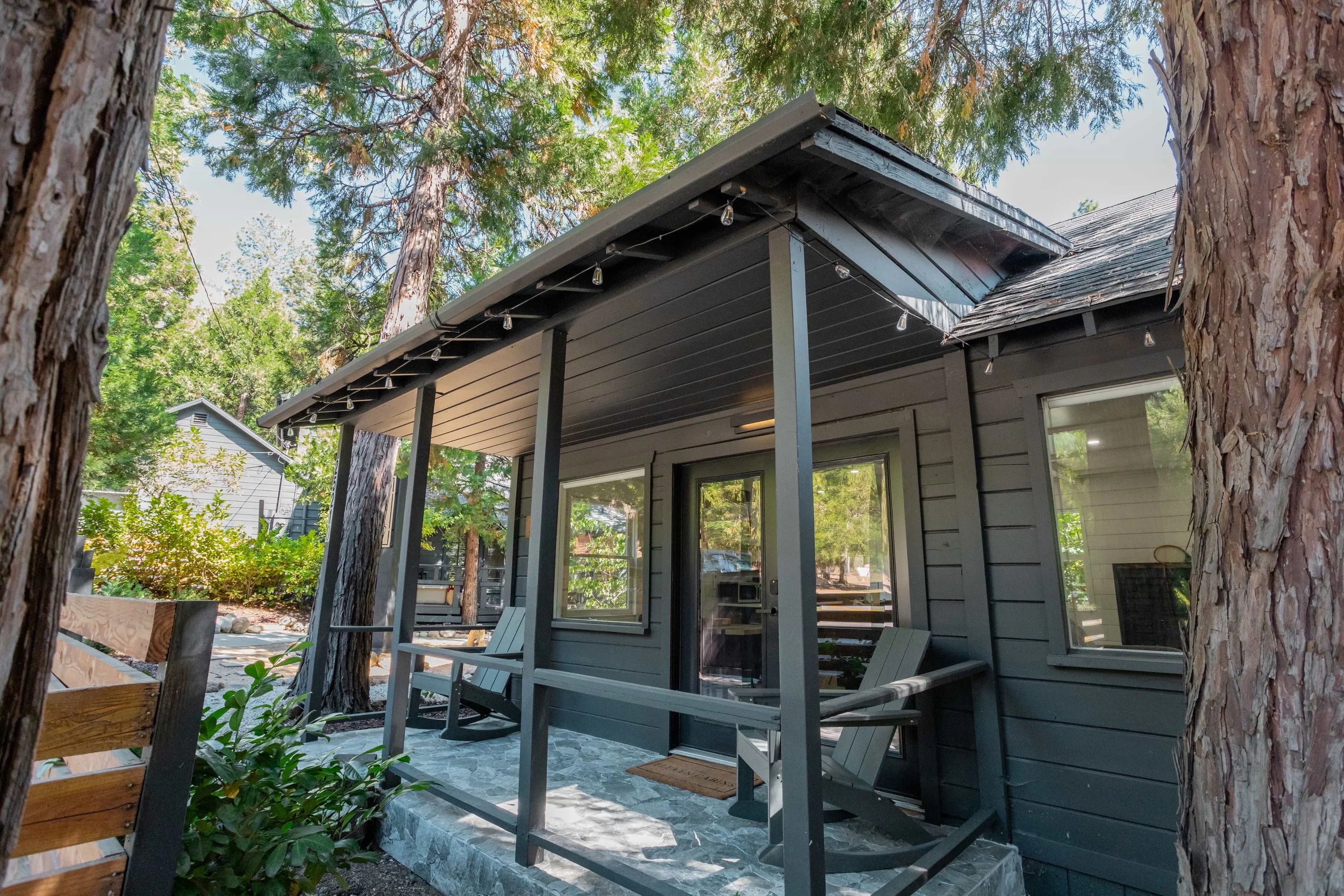 A cozy house with a small porch, two rocking chairs, surrounded by tall trees and greenery in a suburbThe Pinetree Hotel Idyllwild:  a - Idyllwild California, cozy cabin, mountain resort, mountain getaway Modern bathroom in cabin 1 wian neighborhood.