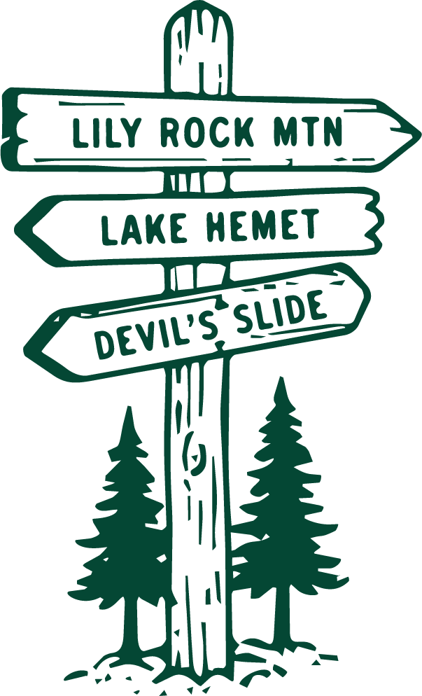 A stylized green wooden signpost with four directional arrows pointing to Lily Rock Mountain, Middle Lake Hemet, Devil's Slide, and an unlisted location, set against a black background with pine trees below.