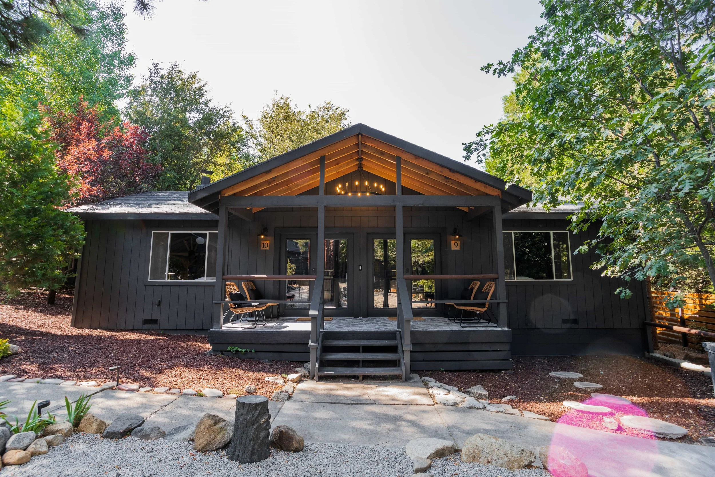 Front view of a modern black house with a covered porch, wooden steps, and two chairs, surrounded by trees and landscaping.