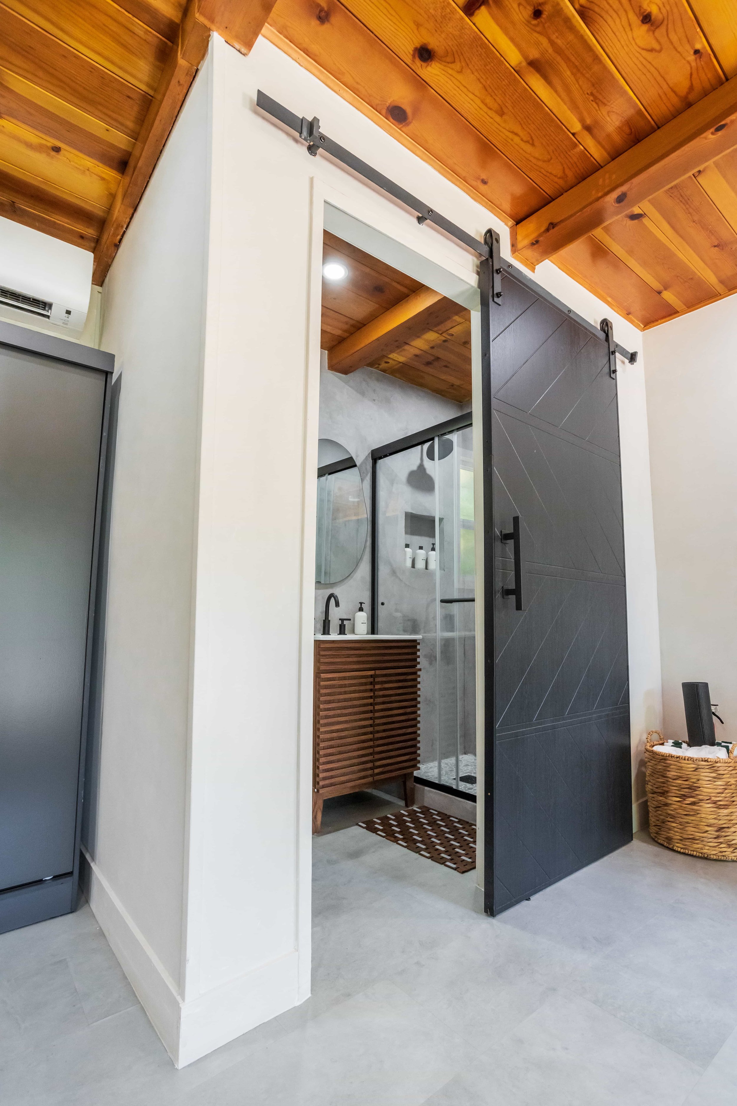Modern bathroom with a black sliding barn door, wooden ceiling, and a vanity with a round mirror and a glass shower enclosure.