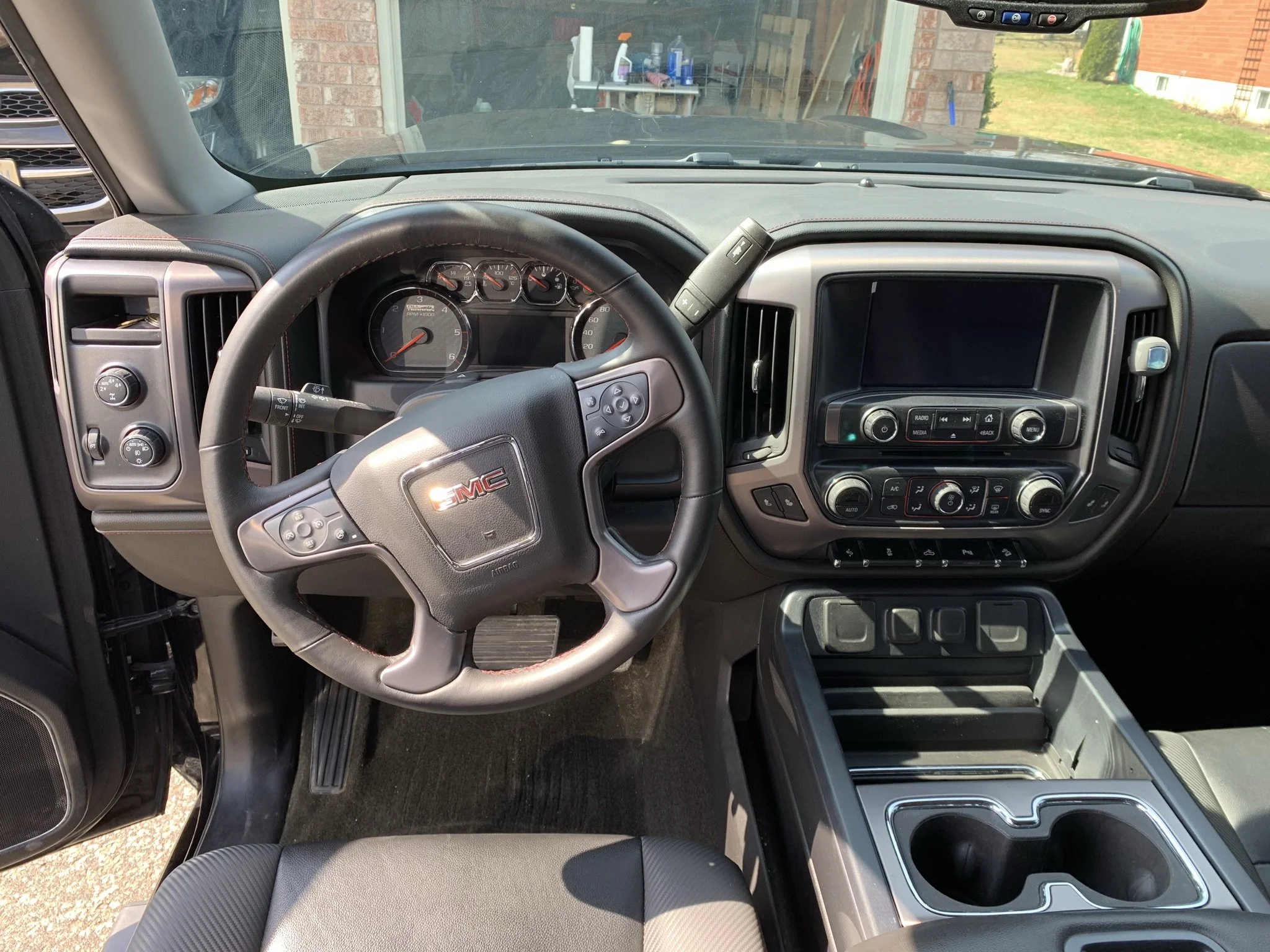 The interior of a GMC vehicle showing the steering wheel with GMC logo, dashboard gauges, center console with a touchscreen display, climate control, and gear shift area.
