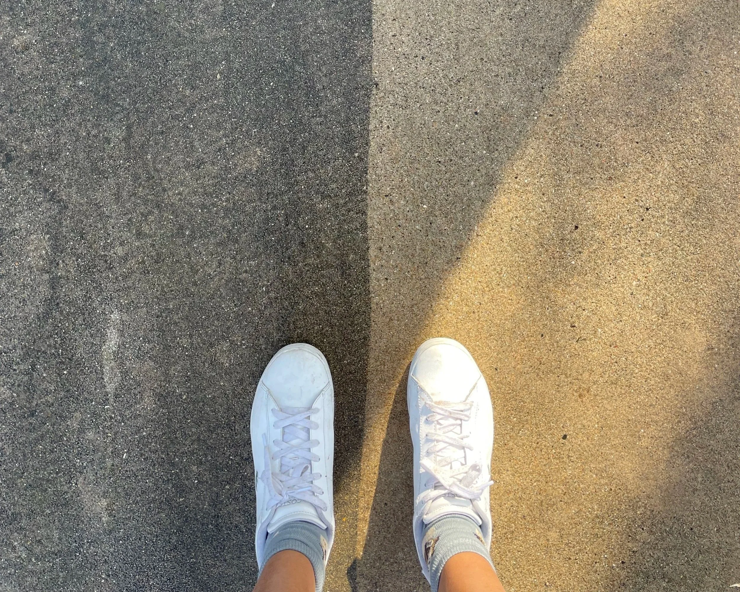 Pair of white sneakers on concrete, showing dirty vs clean driveway (one side is dark, one side is lighter)