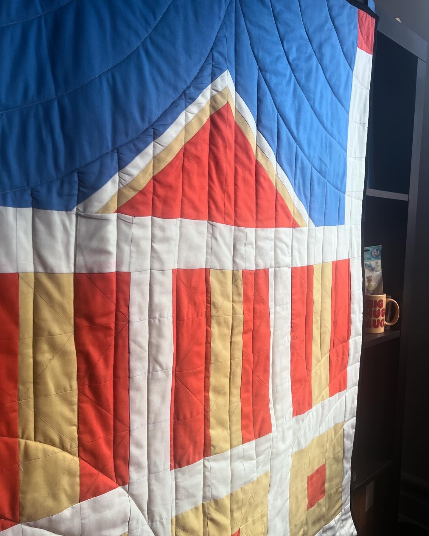 Close-up of a quilt with a colorful geometric pattern including red, yellow, white, and blue fabric squares and triangles.