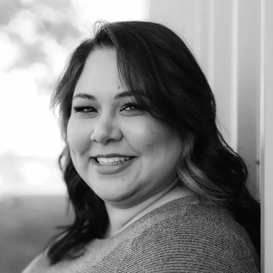 A woman with dark hair smiling while leaning against a wall.