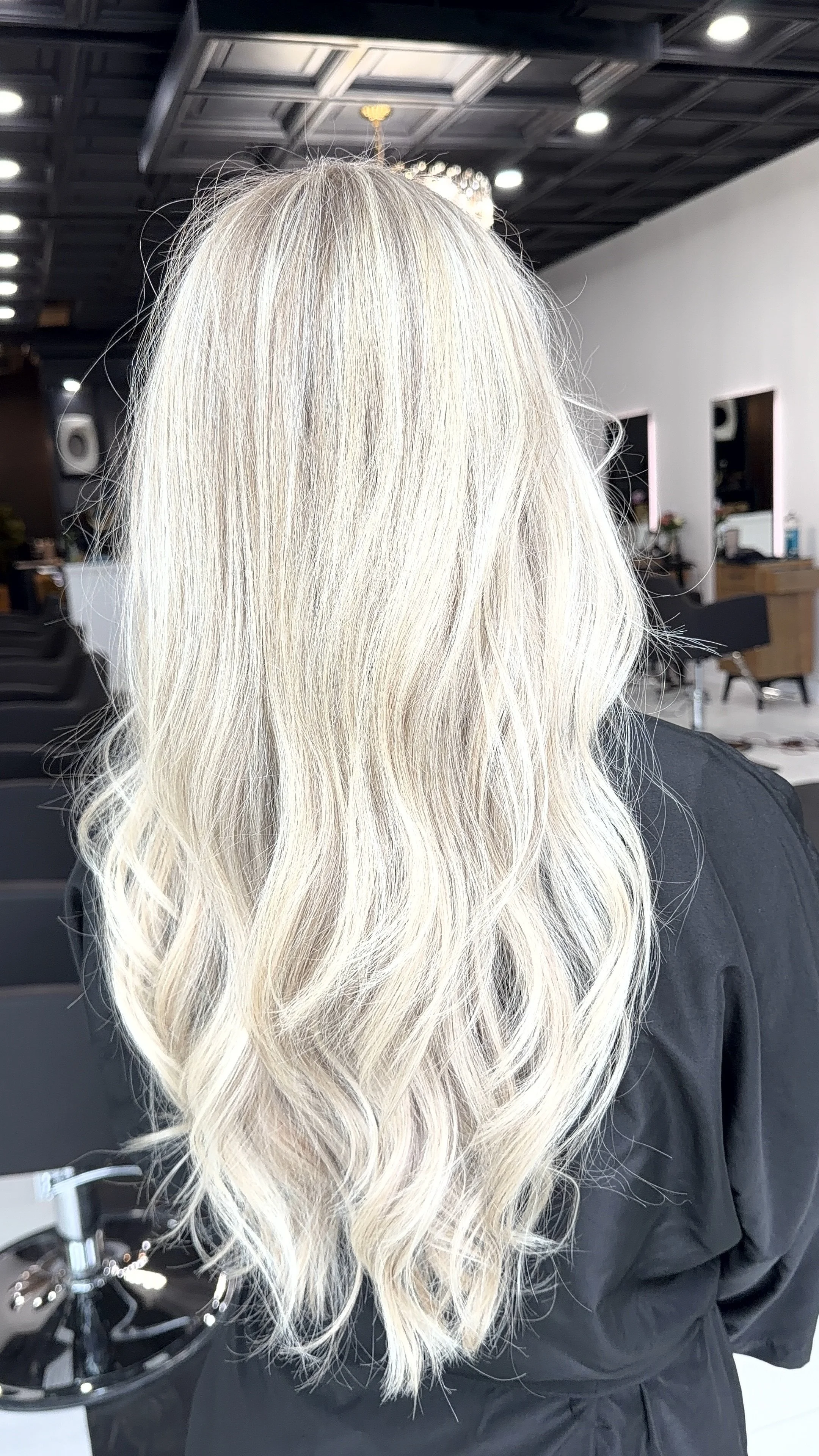 Back of a woman with long, wavy, platinum blonde hair in a hair salon.