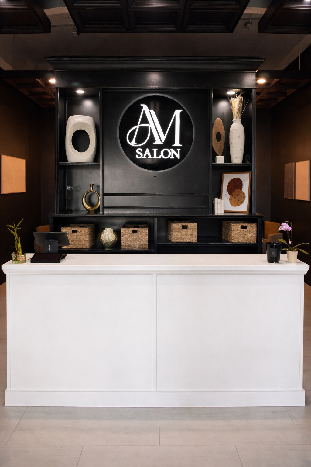 Front desk area at A M Salon with decorative items and framed artwork, featuring a black background with illuminated white logo.