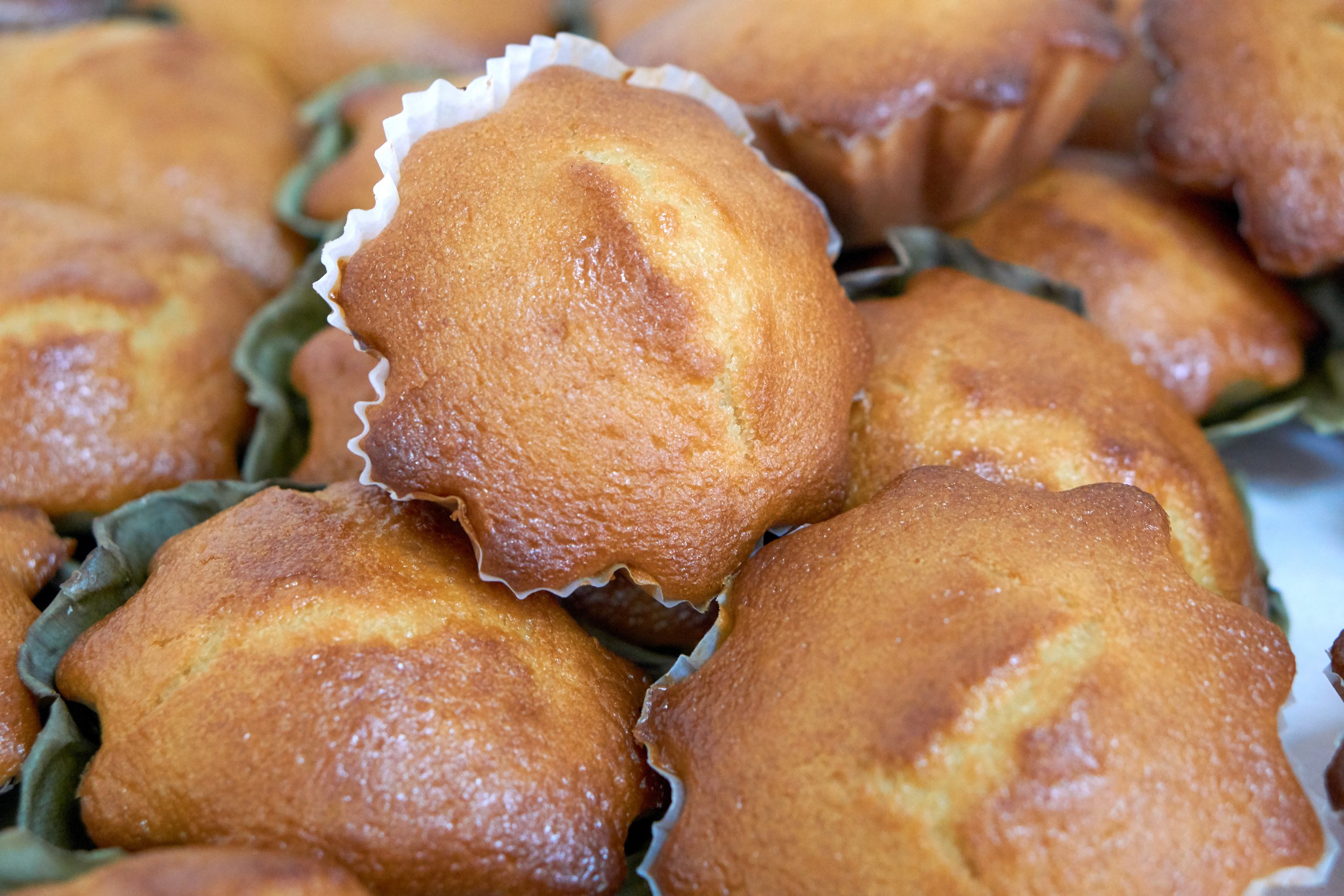Close-up of golden-brown muffins with a slightly crispy surface, some in paper cups, stacked together.