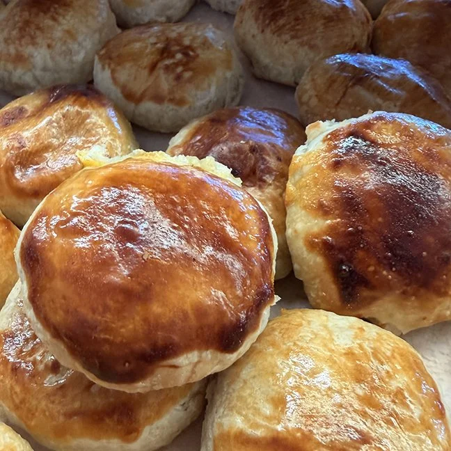 Close-up of freshly baked bread rolls with golden brown crusts. Some rolls have shiny, smooth tops, while others have a slightly cracked surface.
