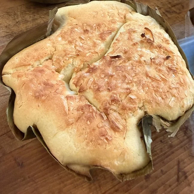 A baked bread with a golden-brown crust, shaped irregularly, placed on a wooden surface with a piece of parchment paper underneath.