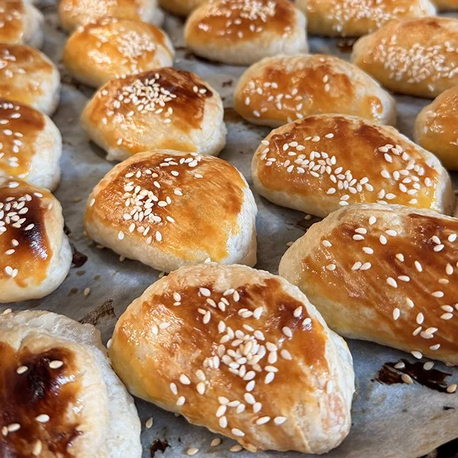 Fresh baked bread rolls with a shiny glaze and sprinkled with sesame seeds on top.