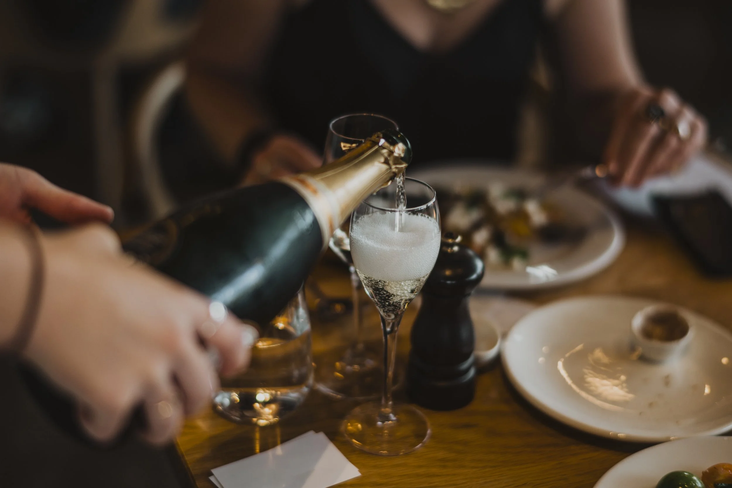 Person pouring champagne into a glass at a dinner table.