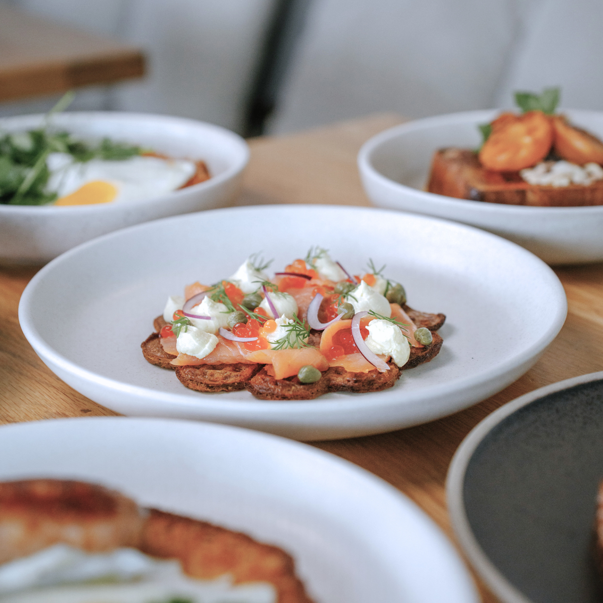 A dish of smoked salmon with dollops of cream cheese, thinly sliced red onions, capers, and garnished with dill on a toasted crisp on a white plate.