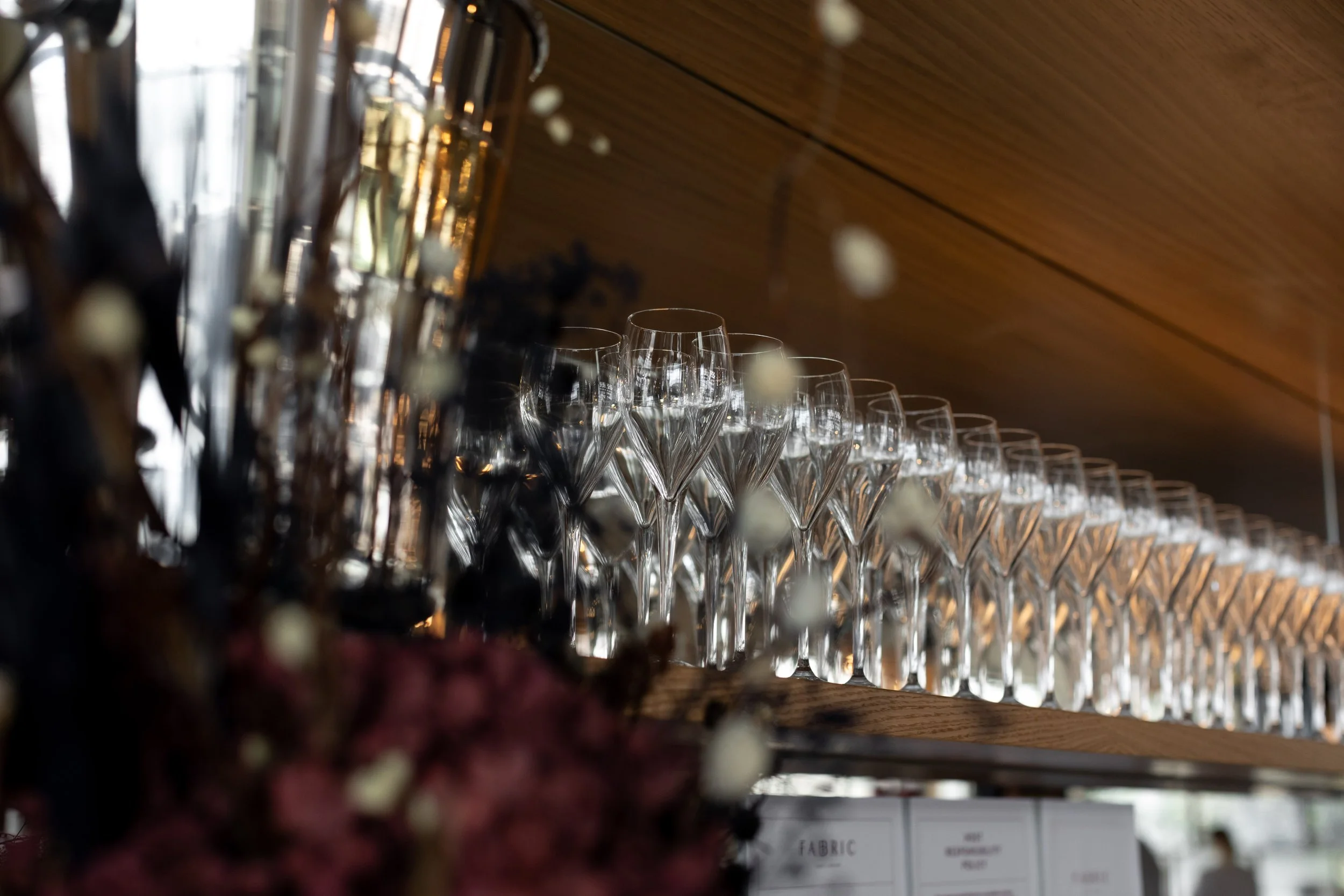 A display of empty wine glasses lined up on a wooden shelf, with a blurred background.