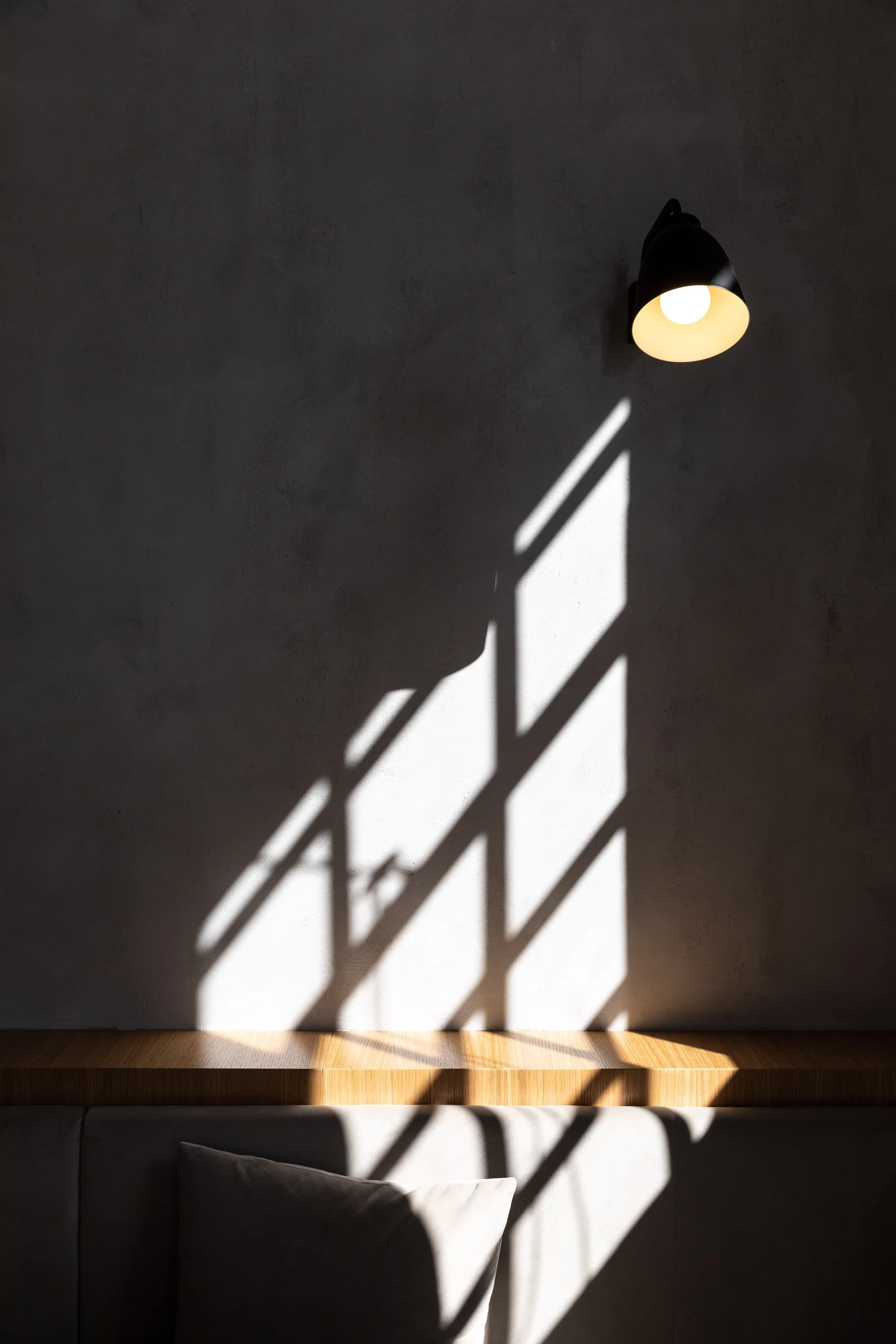 A gray wall with a black wall sconce light fixture casting shadows and light patterns on the wall.