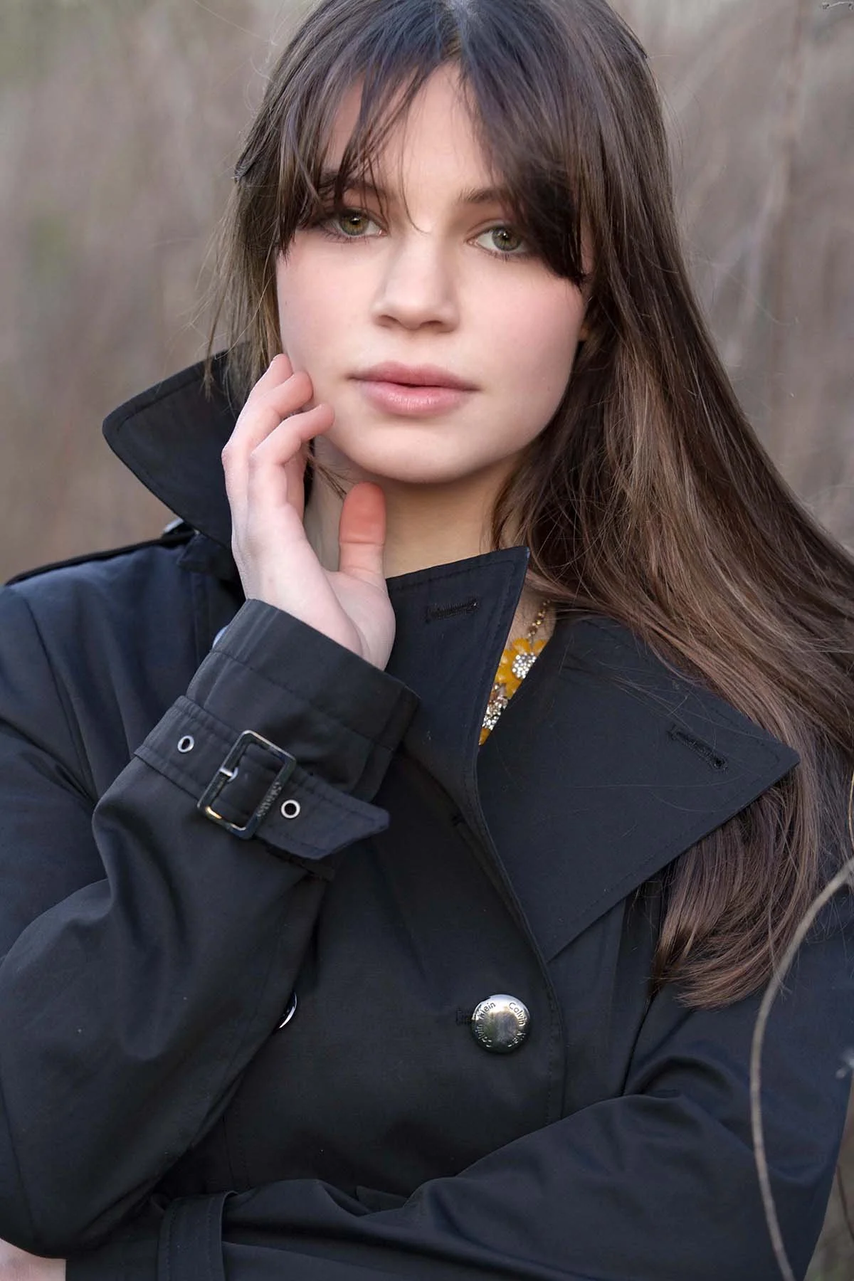 Close-up of a young woman with brown hair and green eyes wearing a black coat outdoors.