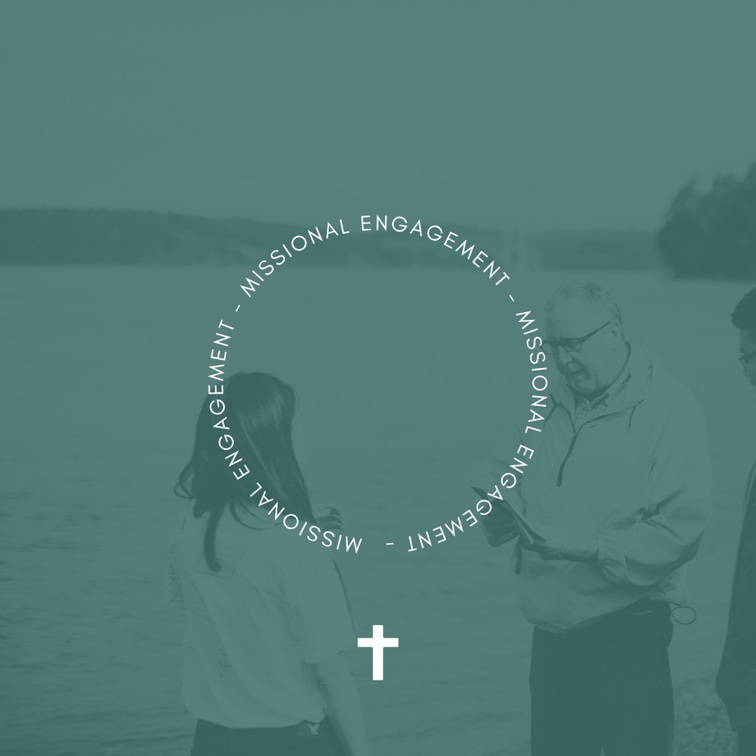 Two people near a body of water, engaged in conversation, with a group of individuals out of focus on the right. Overlaid text reads 'Missional Engagement' in a circle and a cross symbol below.