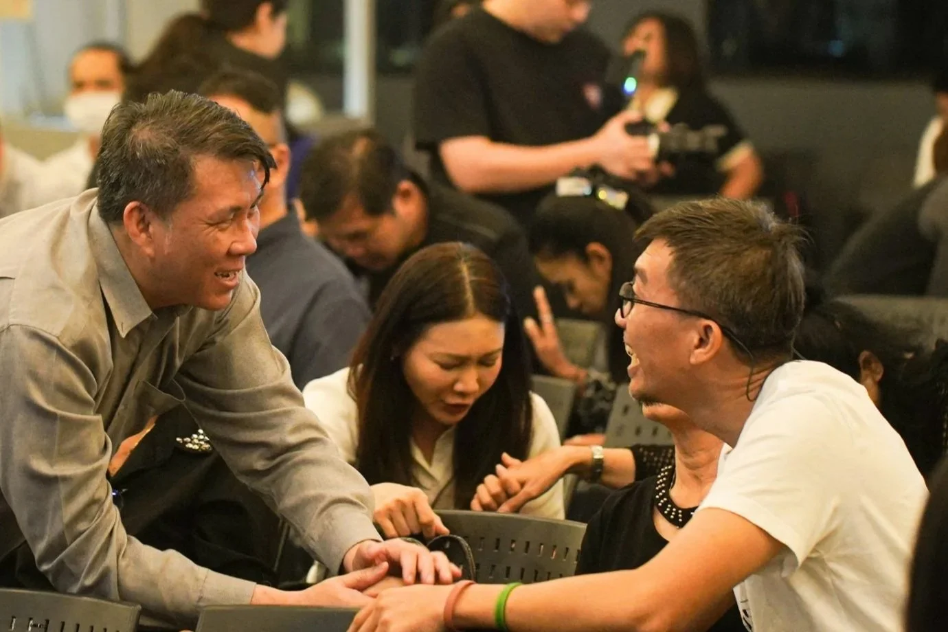 A group of people engaging in lively conversation at a crowded indoor event, with some individuals smiling and gesturing.