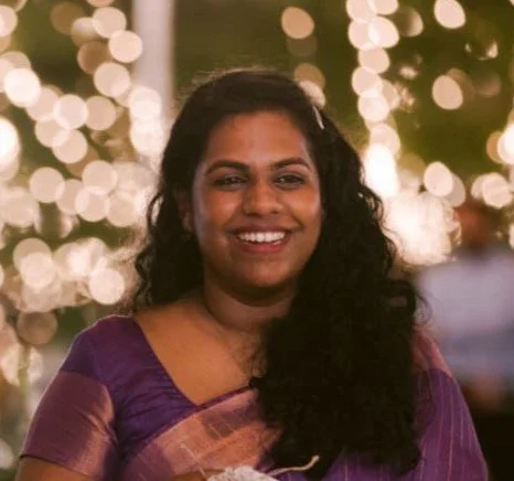 A woman smiling at an event with string lights in the background.