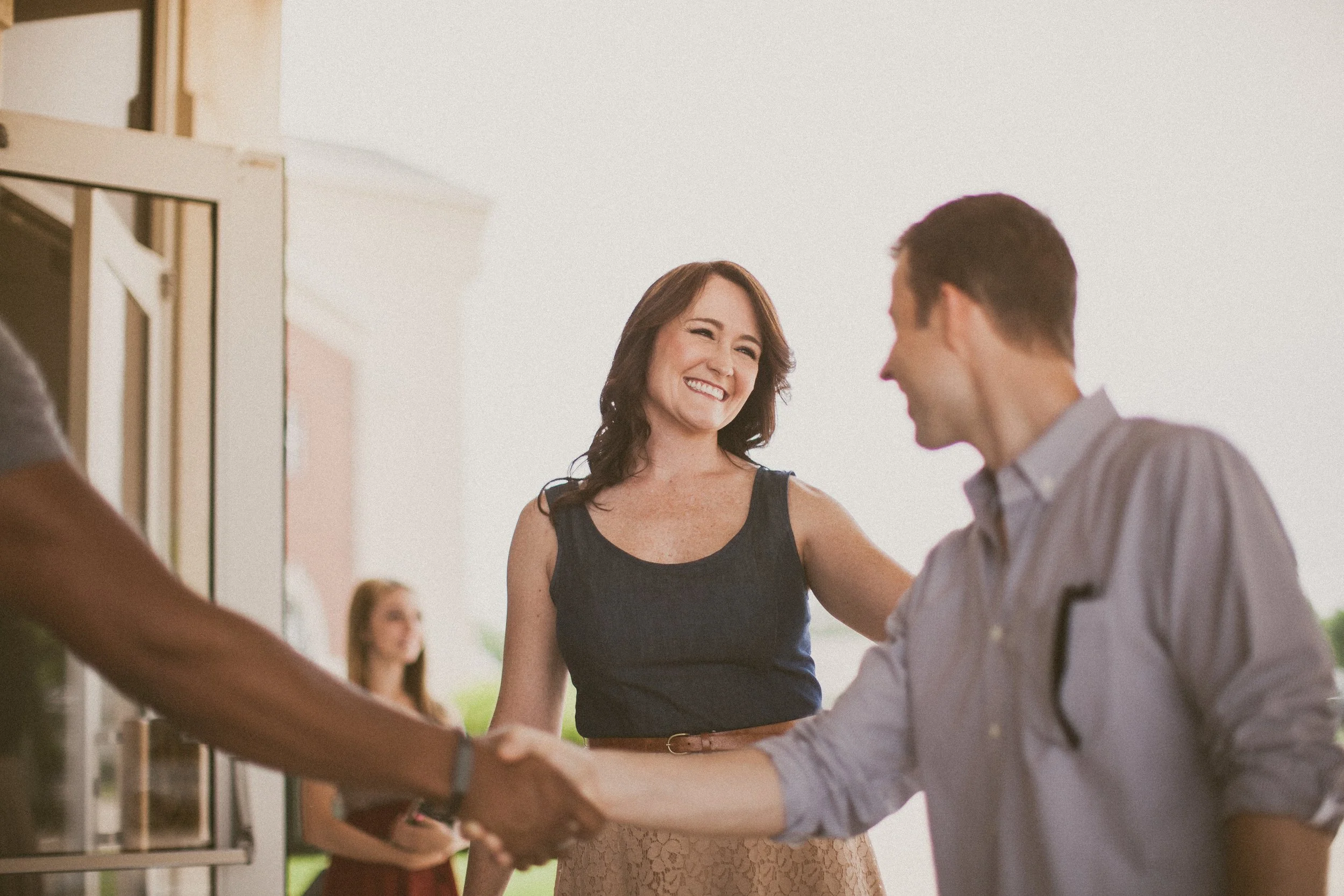 A woman smiling and shaking hands with a man during a social or networking event.