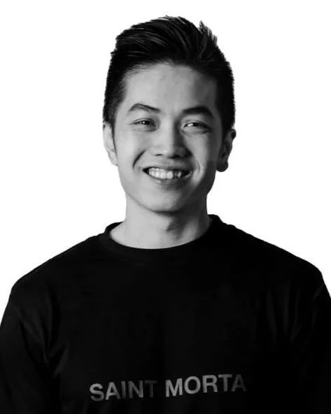 Black and white photo of a smiling young man with short hair, wearing a T-shirt that says 'Saint Morta'.