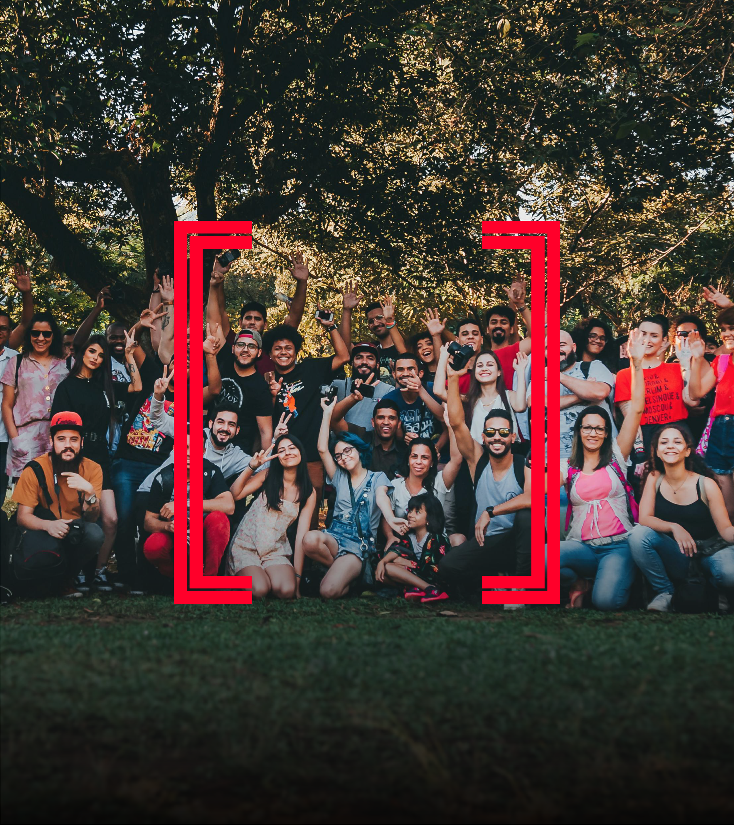 A group of diverse people posing and smiling outdoors under a large tree during daytime.
