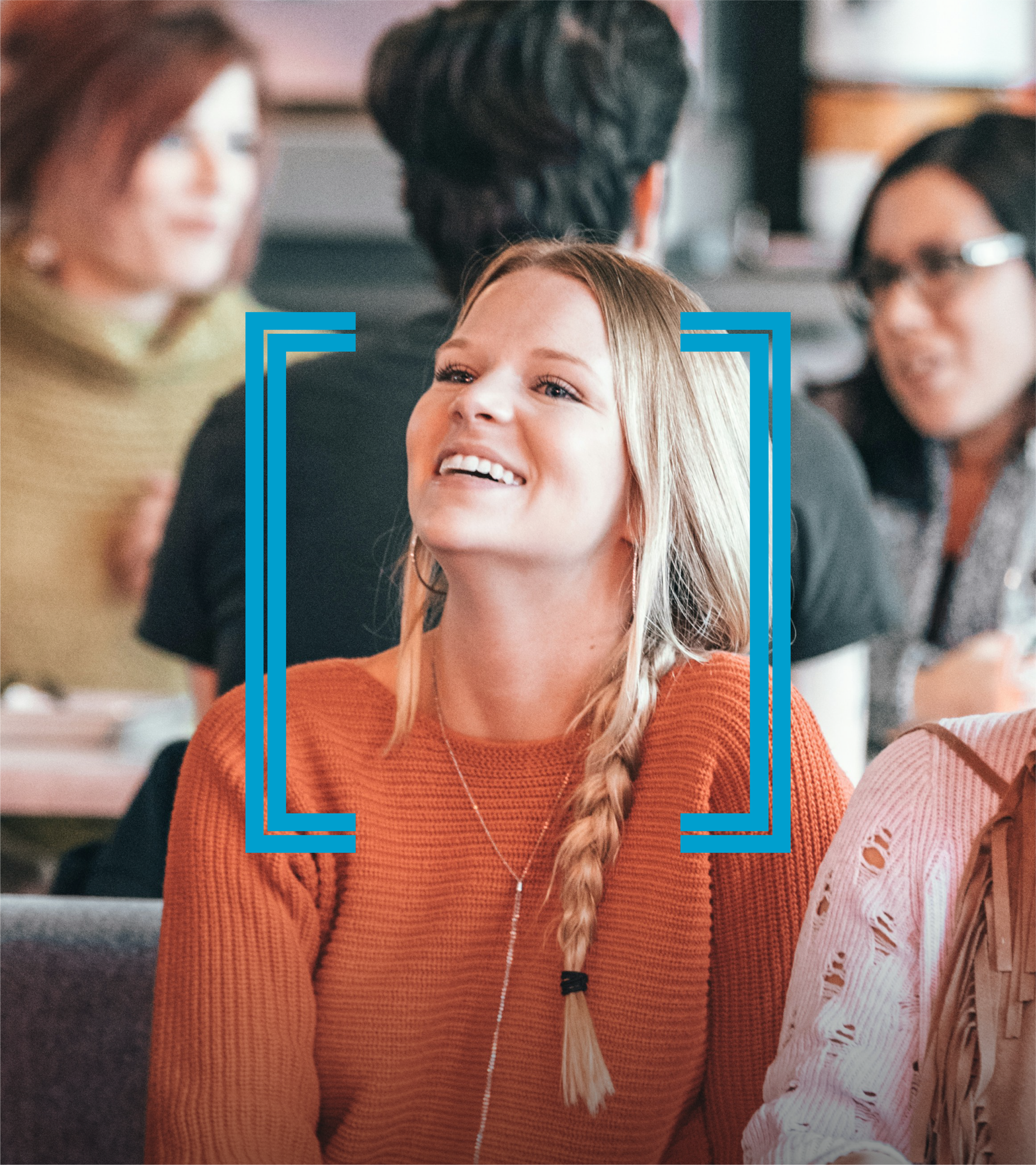 Smiling woman with blonde hair wearing an orange sweater sitting at a table in a social setting, with other people around her.