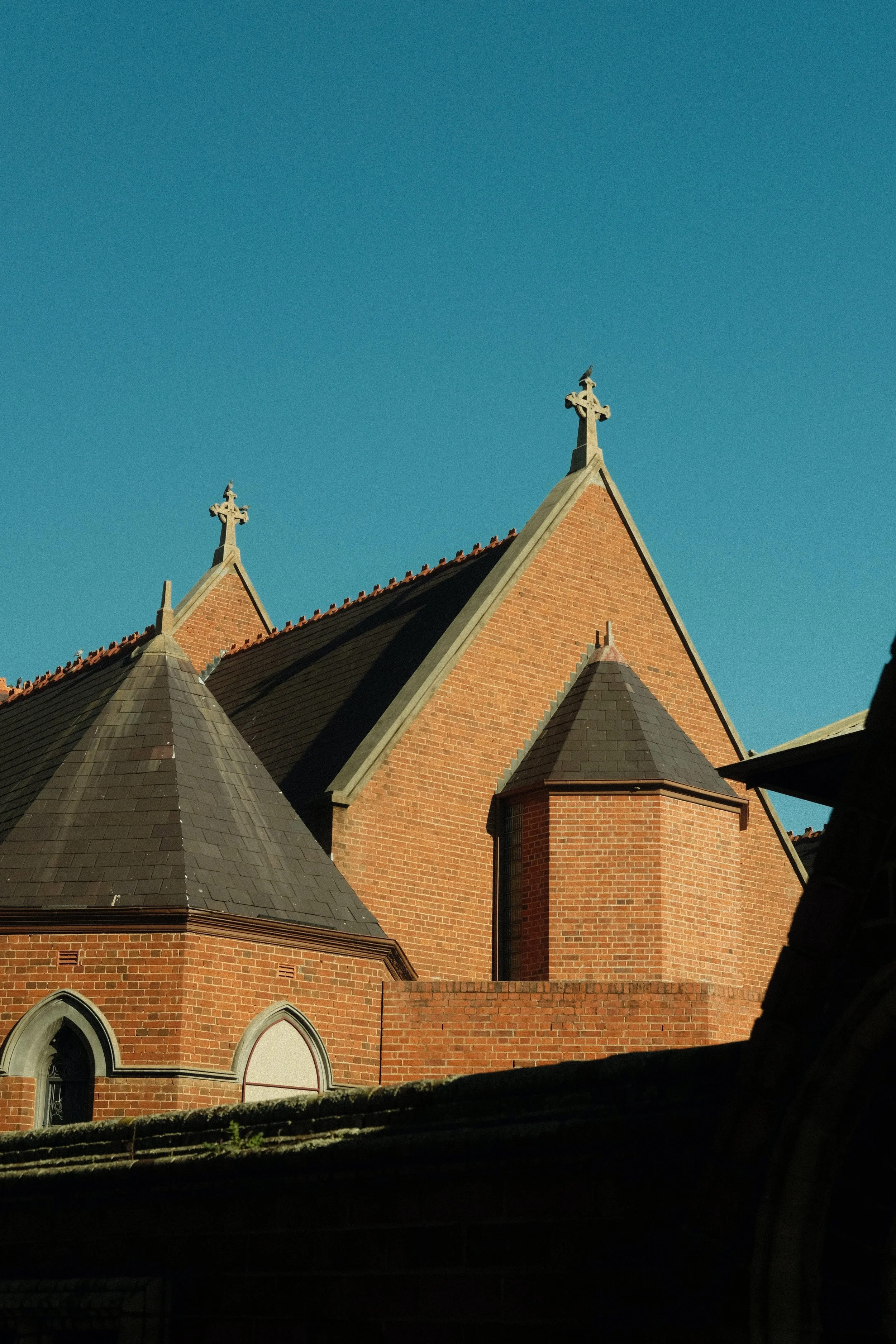A brick church with pointed rooftops and crosses on top, set against a clear blue sky.
