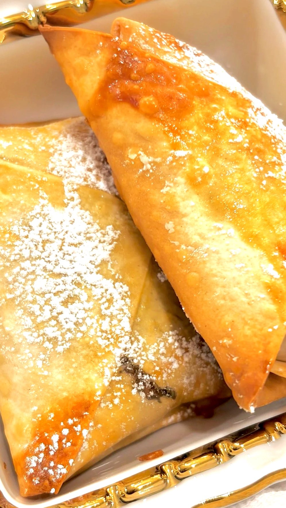 Golden baked folded pastries sprinkled with powdered sugar in a decorative tray.
