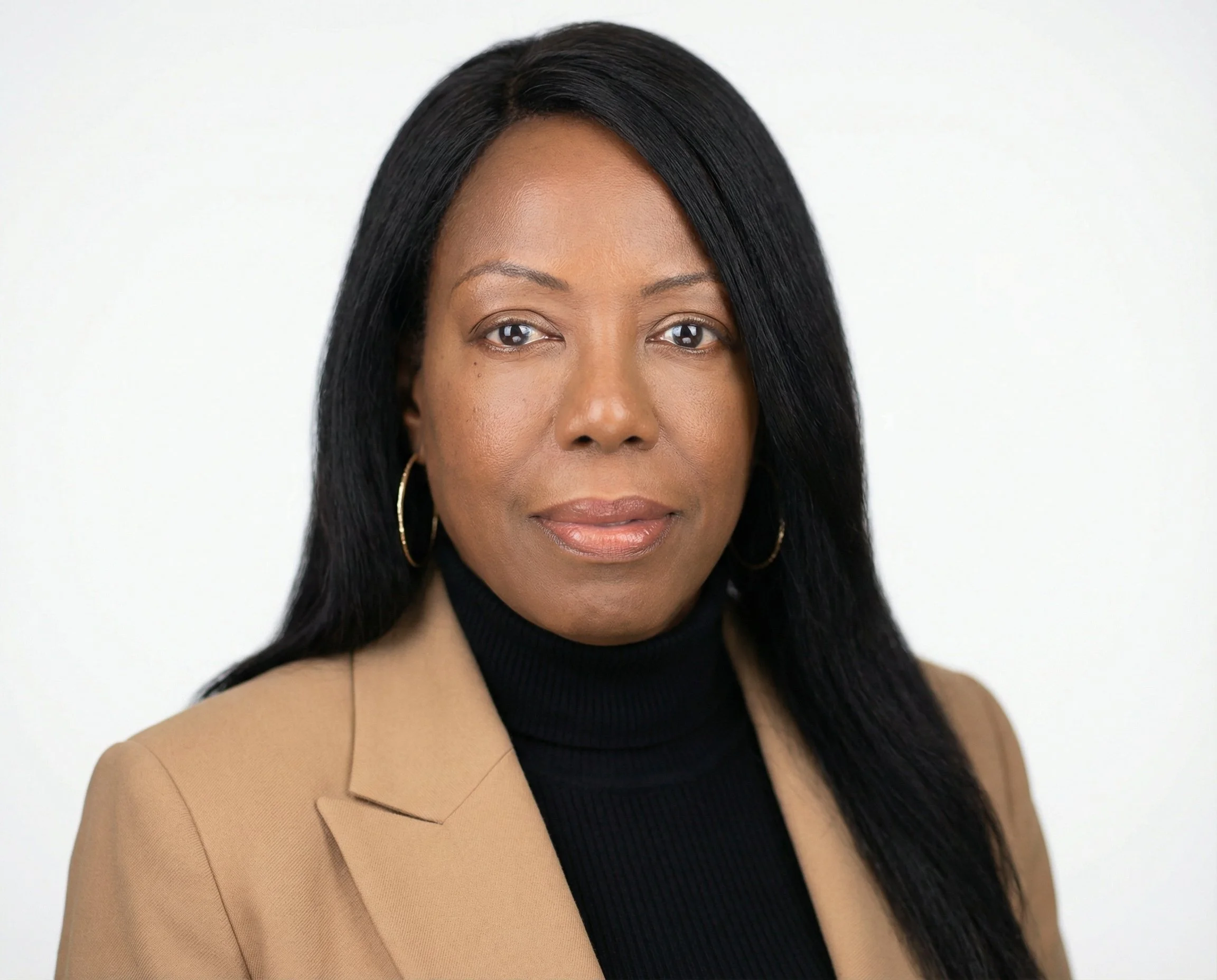 Professional headshot of a woman with long black hair, wearing a tan blazer, black turtleneck, and gold hoop earrings, against a plain white background.