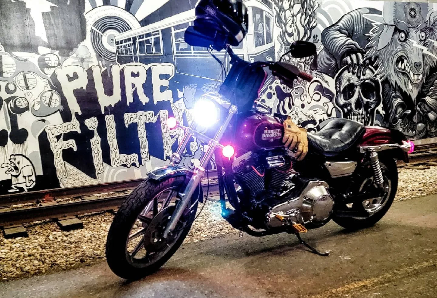 A black Harley Davidson motorcycle parked in front of a black and white graffiti mural with the words "PURE FEELING" and various skull and animal illustrations.