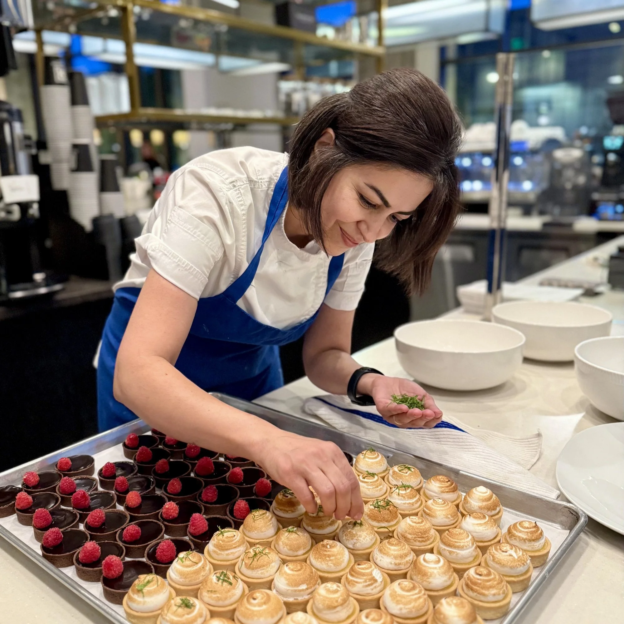 Chef smiling as she puts green mint sprigs on top of lemon tarts
