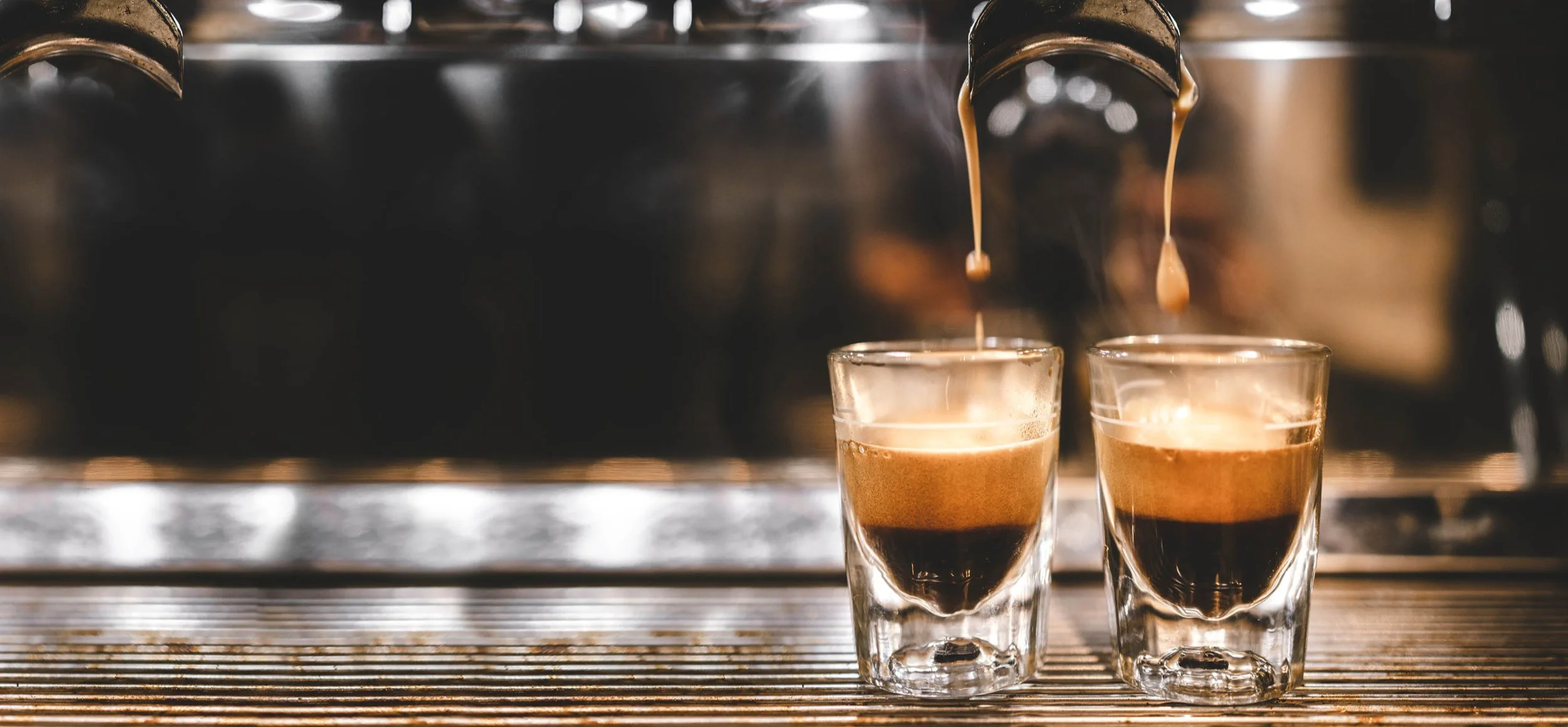 Close up of espresso dripping into two Gibraltar size shot glasses which are on the espresso machine.