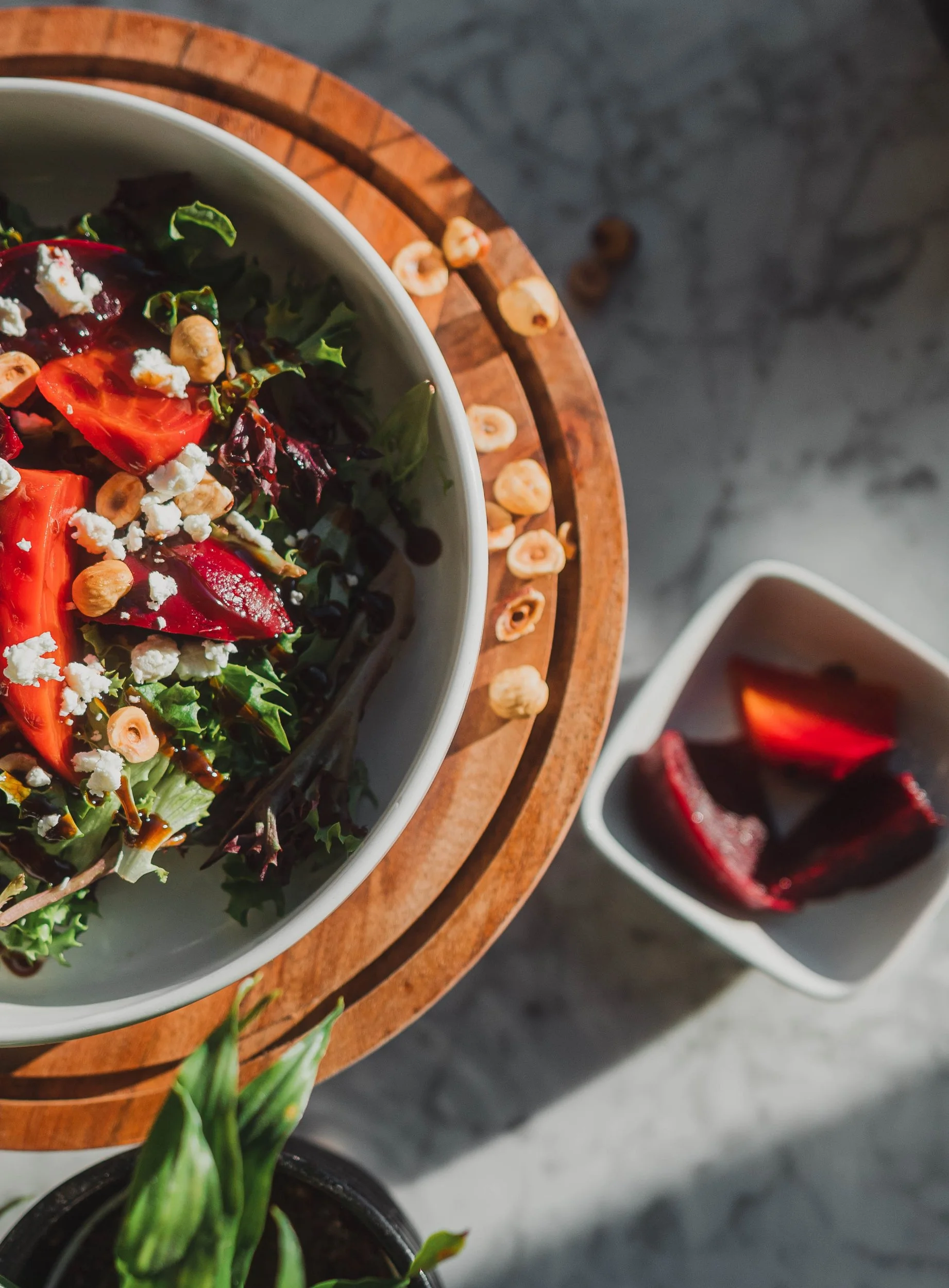 Top down shot of a delicious roasted beet, grain and kale salad. The parceling bowl is on a wooden plate with a few chick pea sprinkled along the edge and a 2nd square small serving plate o f beets off to the side