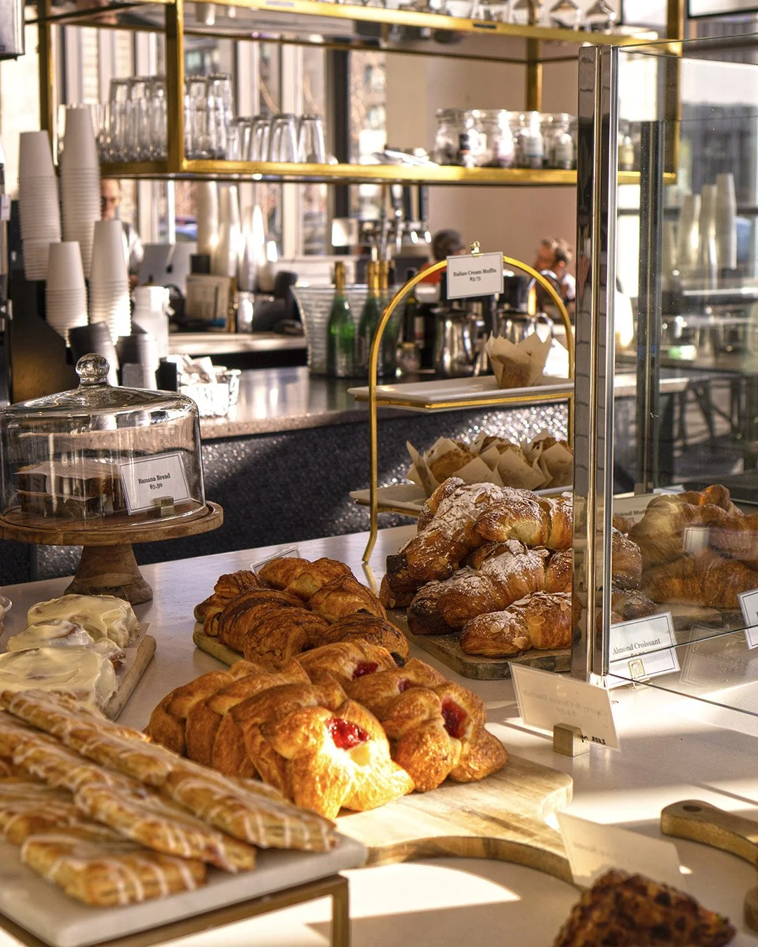 The pastry case at 9+CO early in the morning stocked full of delicious pastries like danishes, almond croissants, scratch made "pop tarts" and muffins in the background. The sun is beaming through the window onto part of the pastries