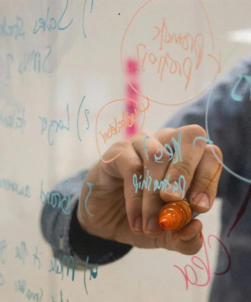 Person writing on a transparent whiteboard with multiple colorful notes and notes in various colors