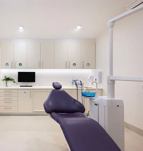 Dental examination chair in a bright, modern dental office with cabinets, a computer, and dental equipment.