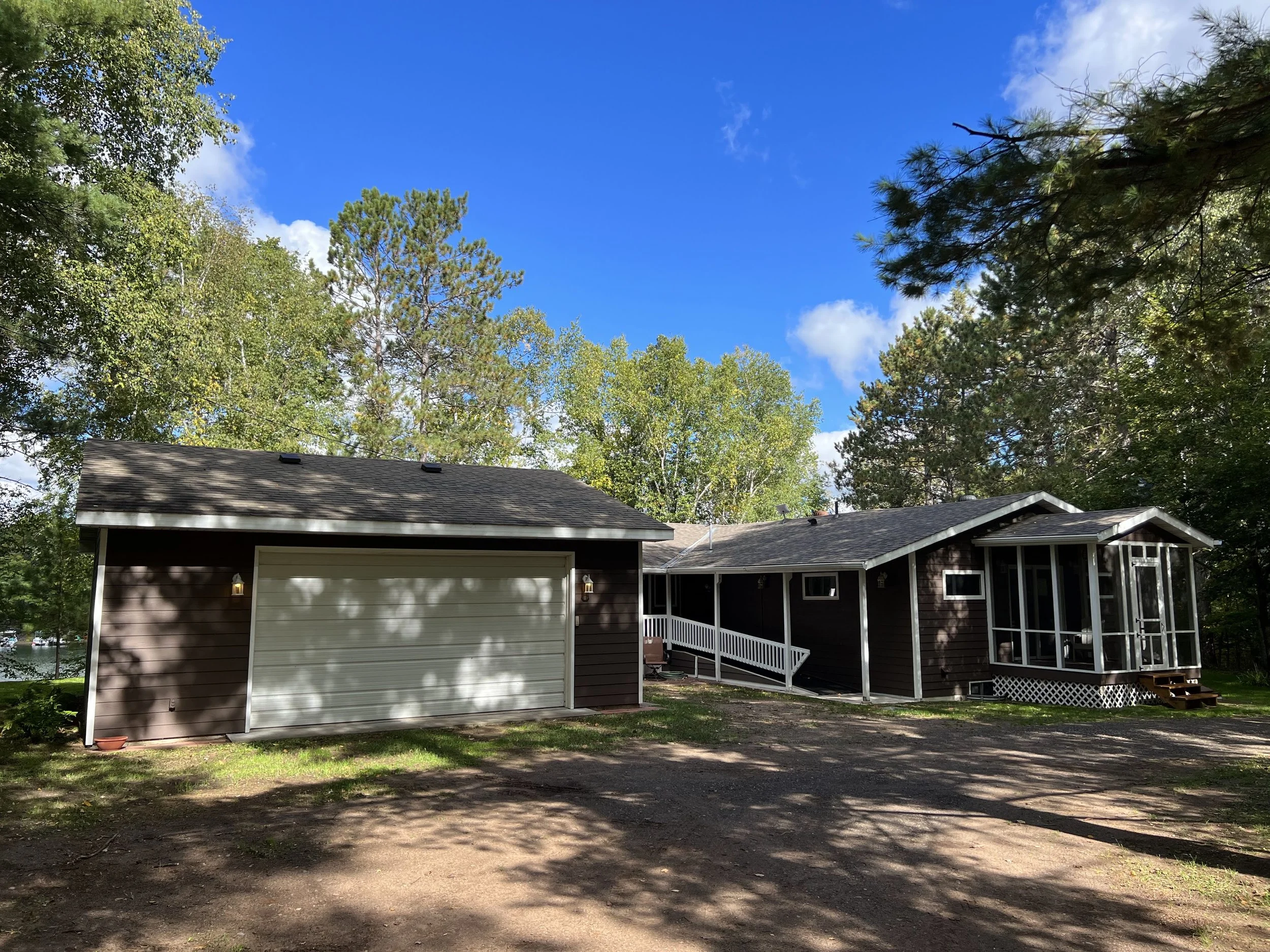 A dark brown house with a screened porch, surrounded by trees under a blue sky with scattered clouds.
